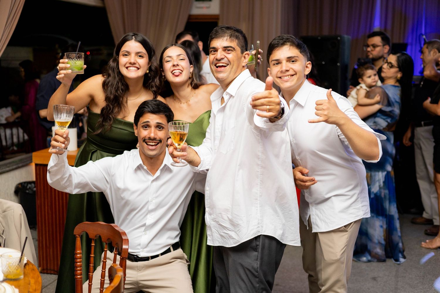 Group of young people smiling and raising glasses in a toast at a festive indoor celebration event.