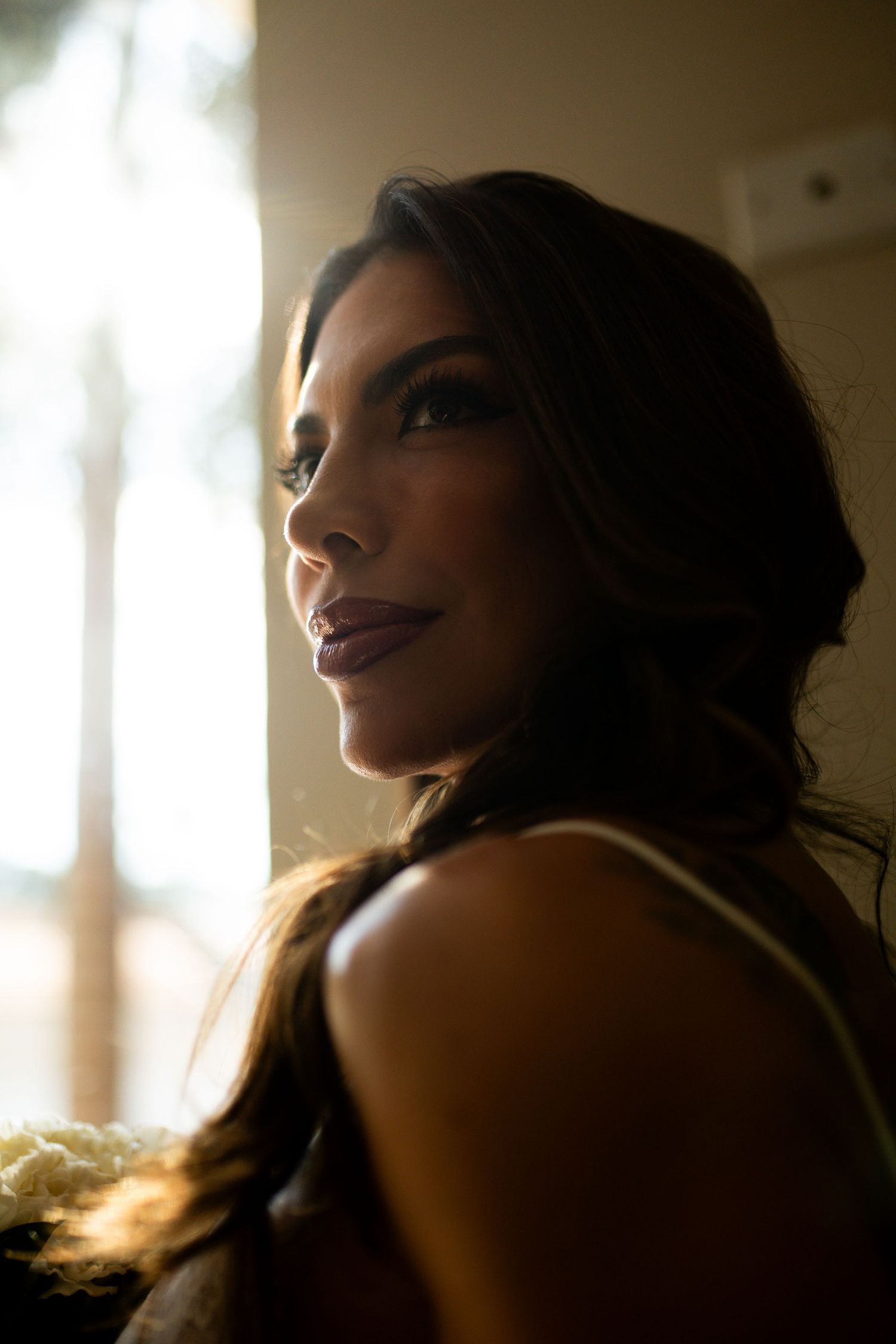 A woman with dark hair and elegant makeup gazes over her shoulder in dramatic backlit portrait photography.
