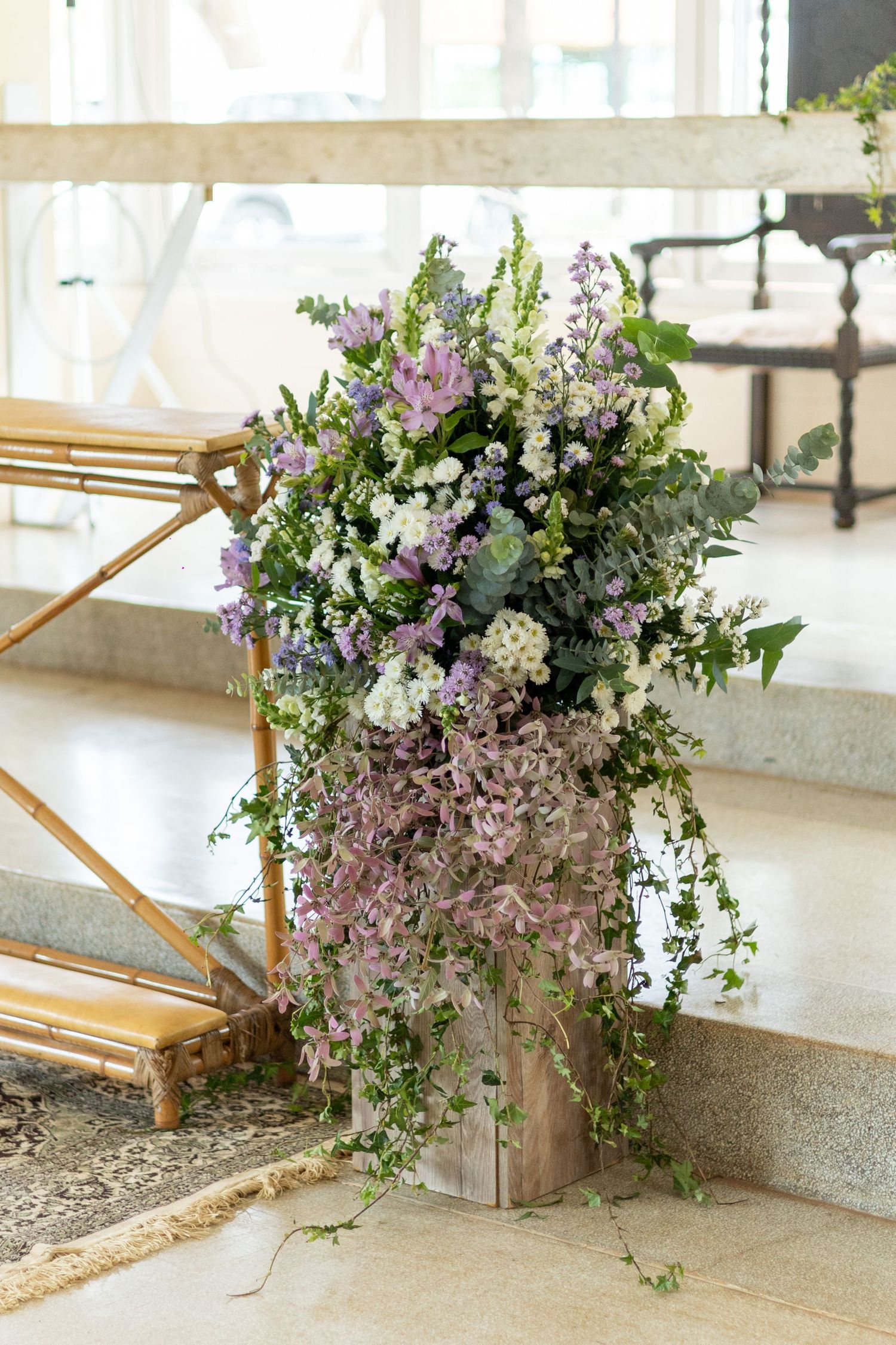Elegant floral arrangement with purple, white, and green flowers in a rustic vase, perfect for wedding decor.