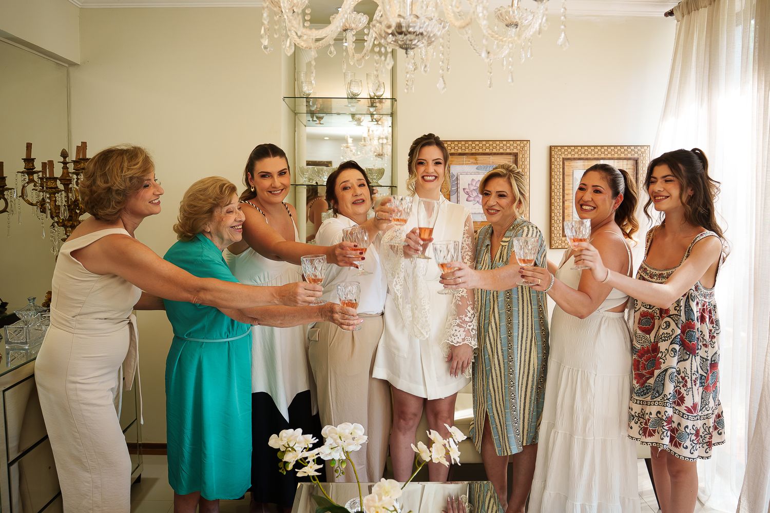 A group of women in elegant attire toasting with champagne glasses at a bridal party celebration indoors.