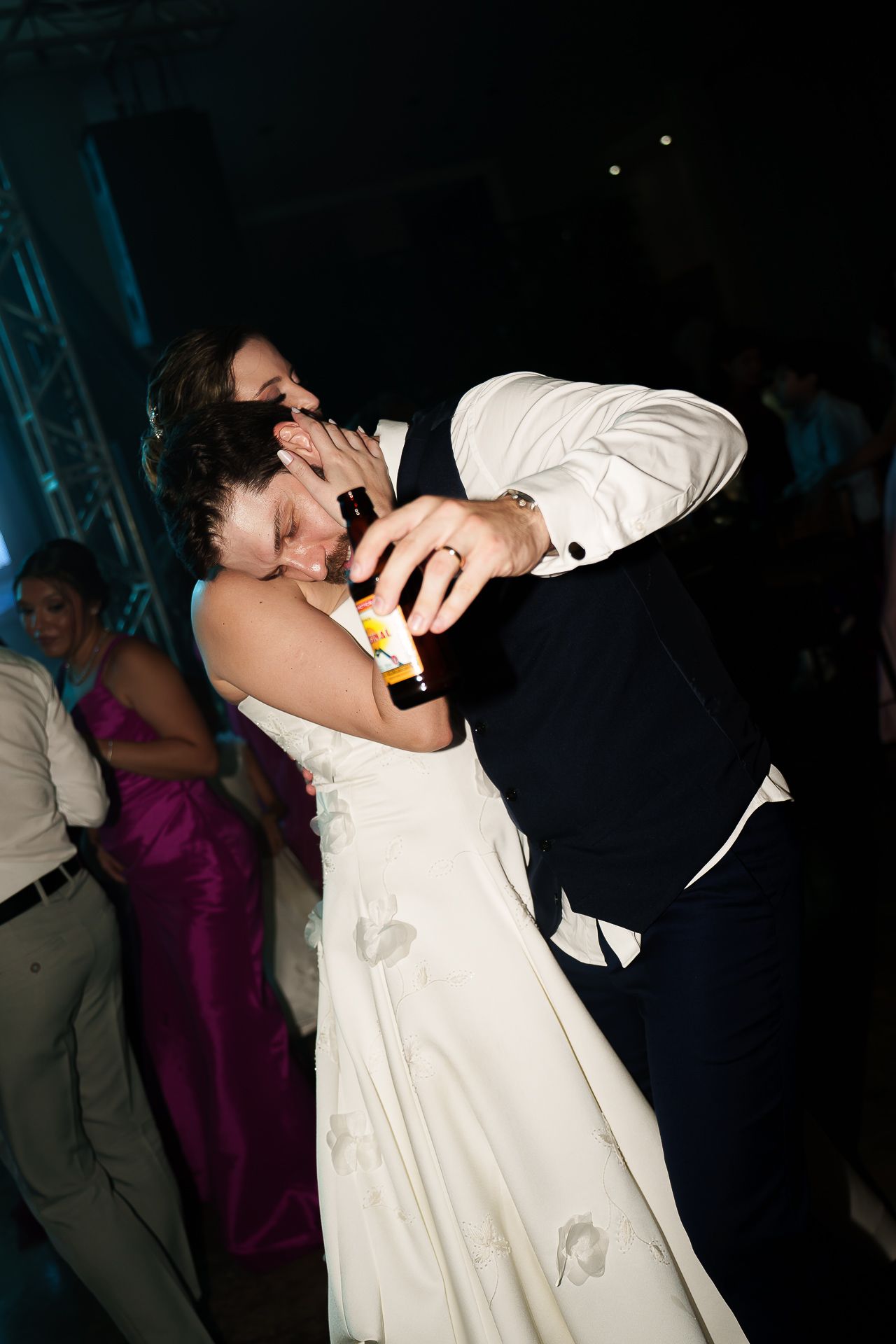 Bride and groom sharing a romantic dance at their wedding reception, groom holding a beer bottle.