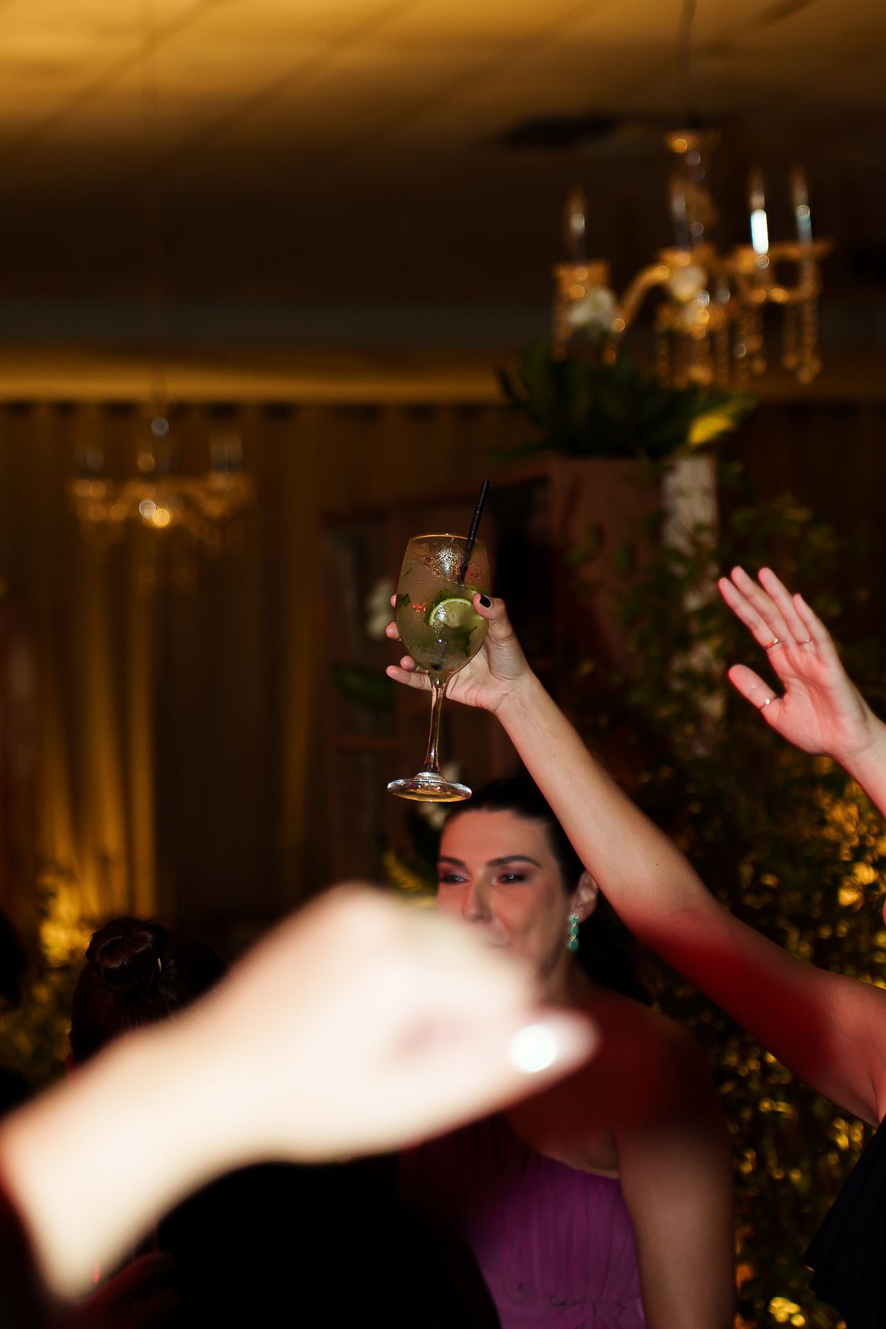 Woman in purple dress raising a cocktail glass in a toast at an elegant indoor party with warm lighting.