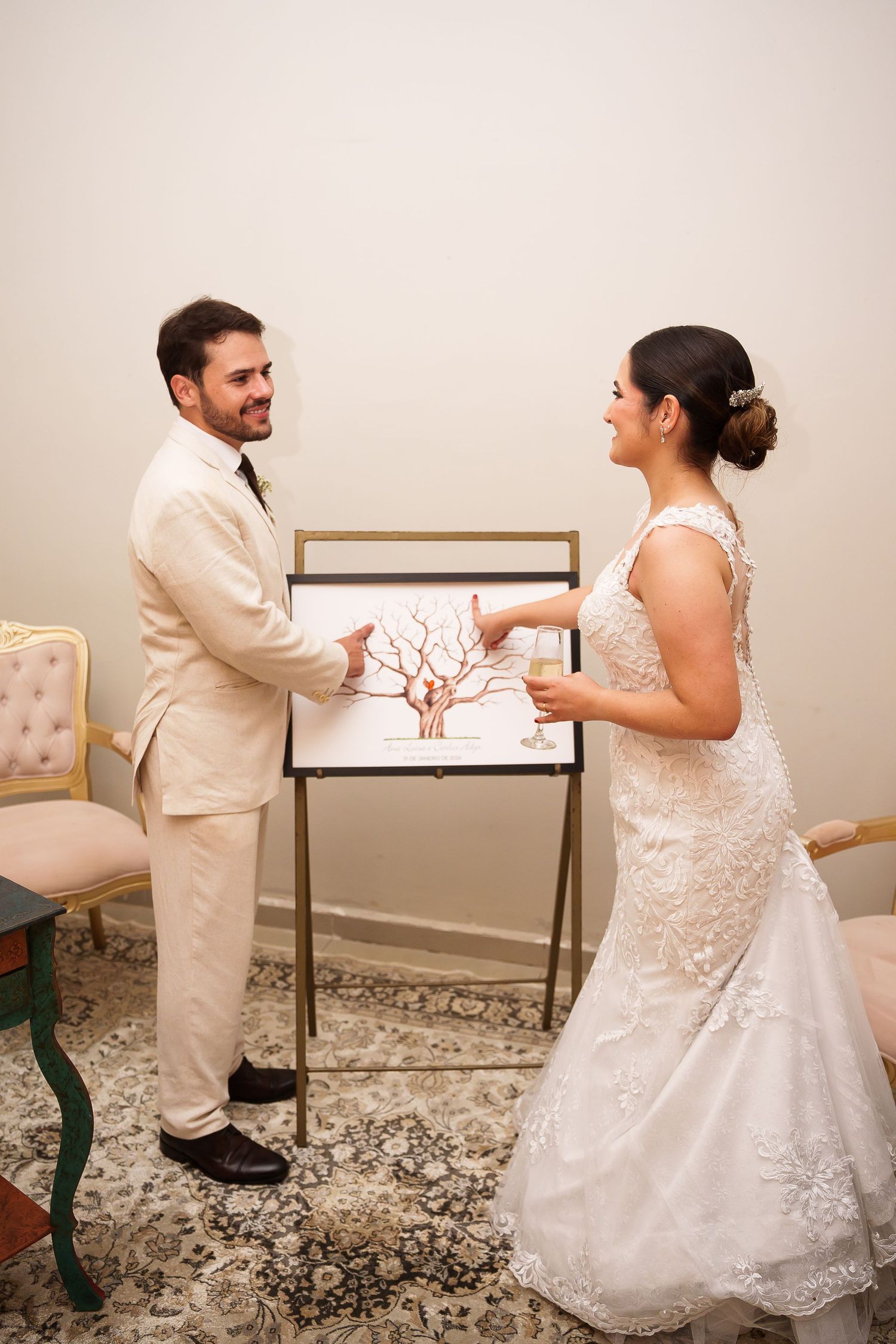 Bride and groom smiling while adding fingerprints to a wedding tree guest book canvas at their reception.