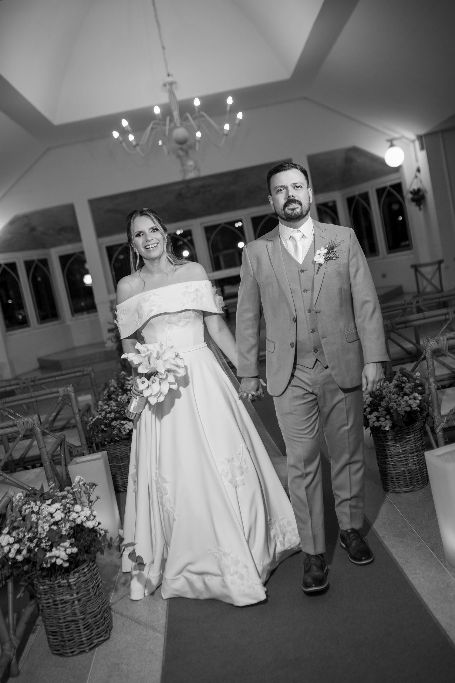 Black and white photo of a bride and groom walking down the aisle in a decorated church after their wedding ceremony.