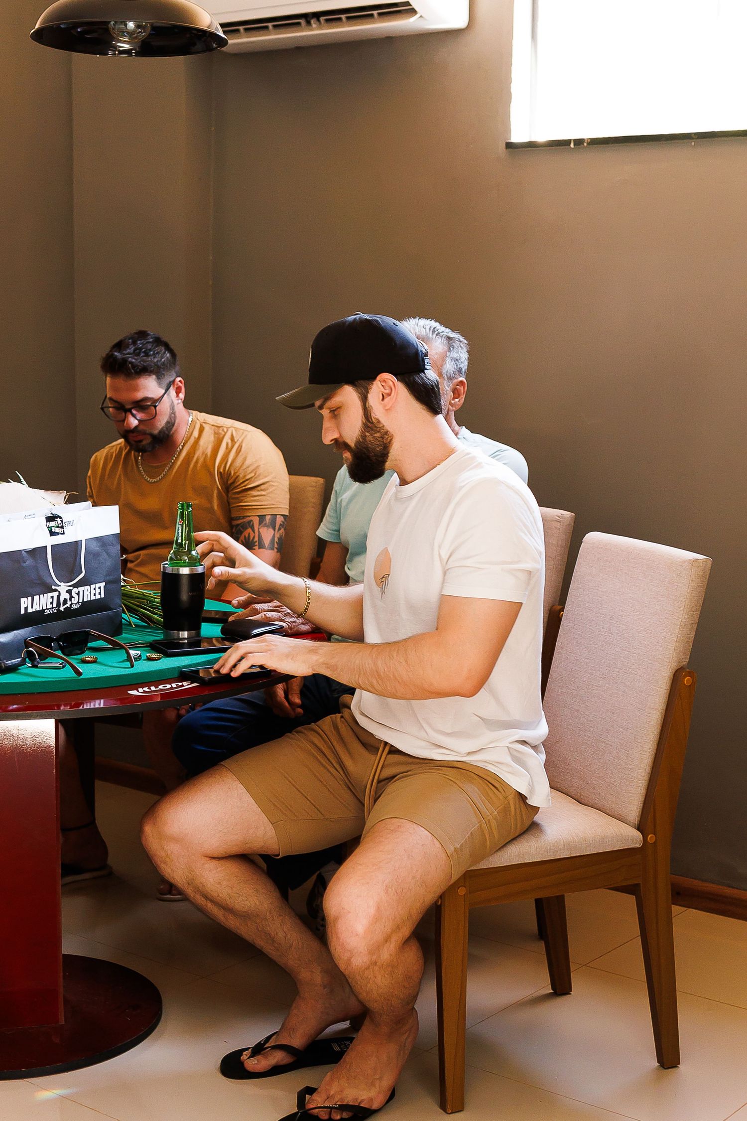 Three men sitting at a round table with laptops and a green bottle, working in a modern office space.