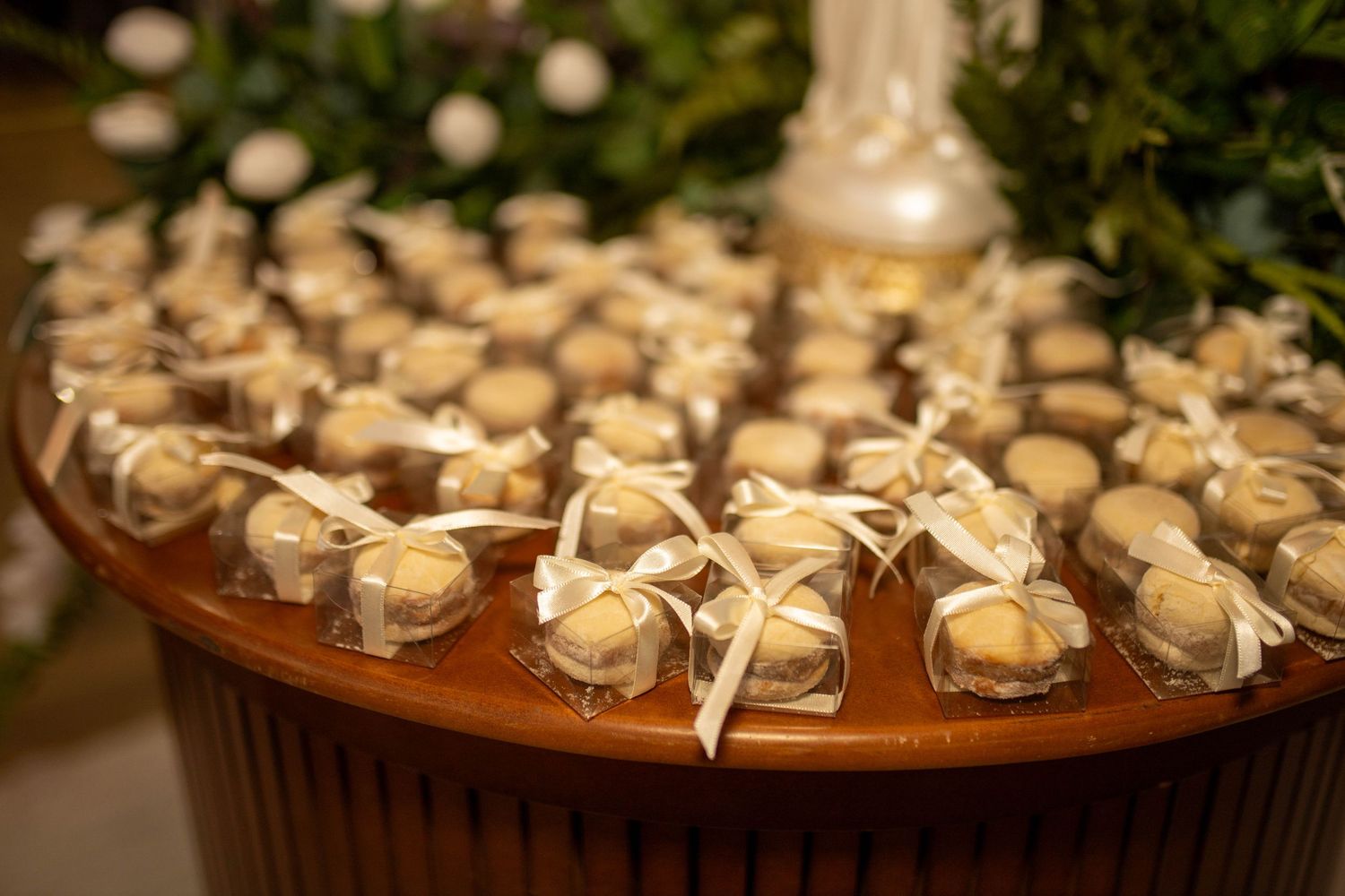 Elegant wedding favor chocolates wrapped in clear packaging with white ribbon bows displayed on a round wooden table.