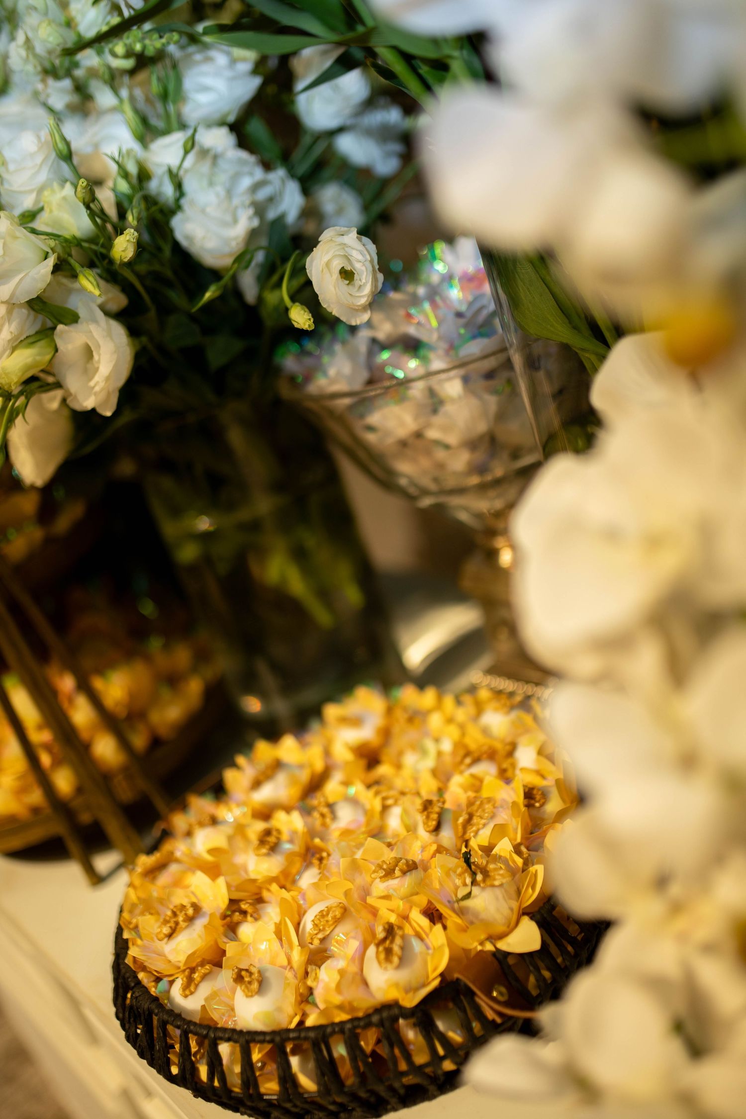 Elegant dessert table with golden petit fours on a decorative tray, surrounded by white roses and crystal glassware.