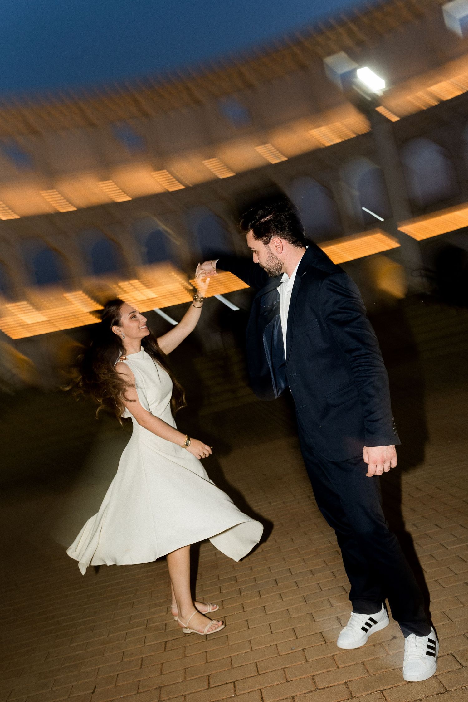 Couple dancing elegantly at night near the Colosseum in Rome, woman in white dress, man in black suit.