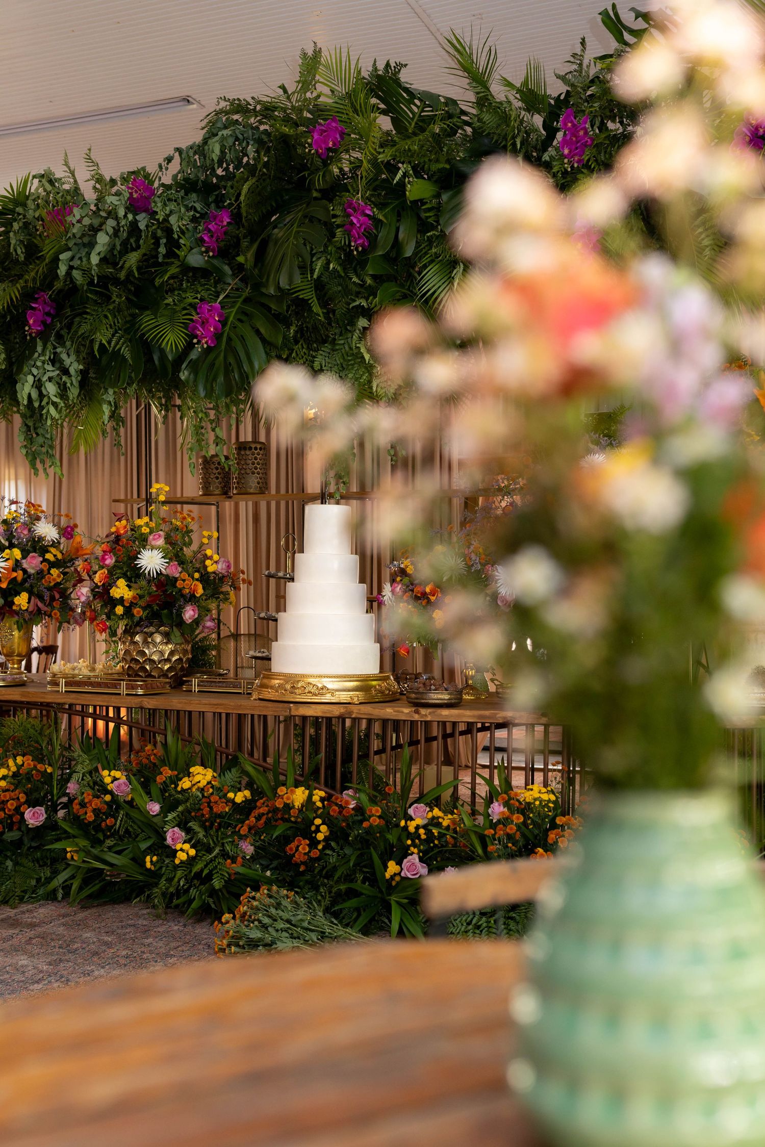 Elegant wedding cake display with lush floral arch, colorful blooms, and tiered white cake on decorated table.