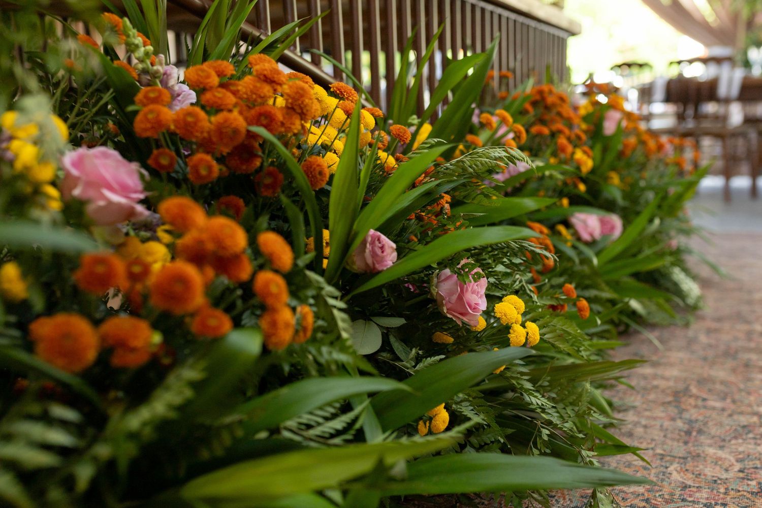 Vibrant arrangement of orange marigolds, pink roses, and tropical greenery lining an outdoor walkway.