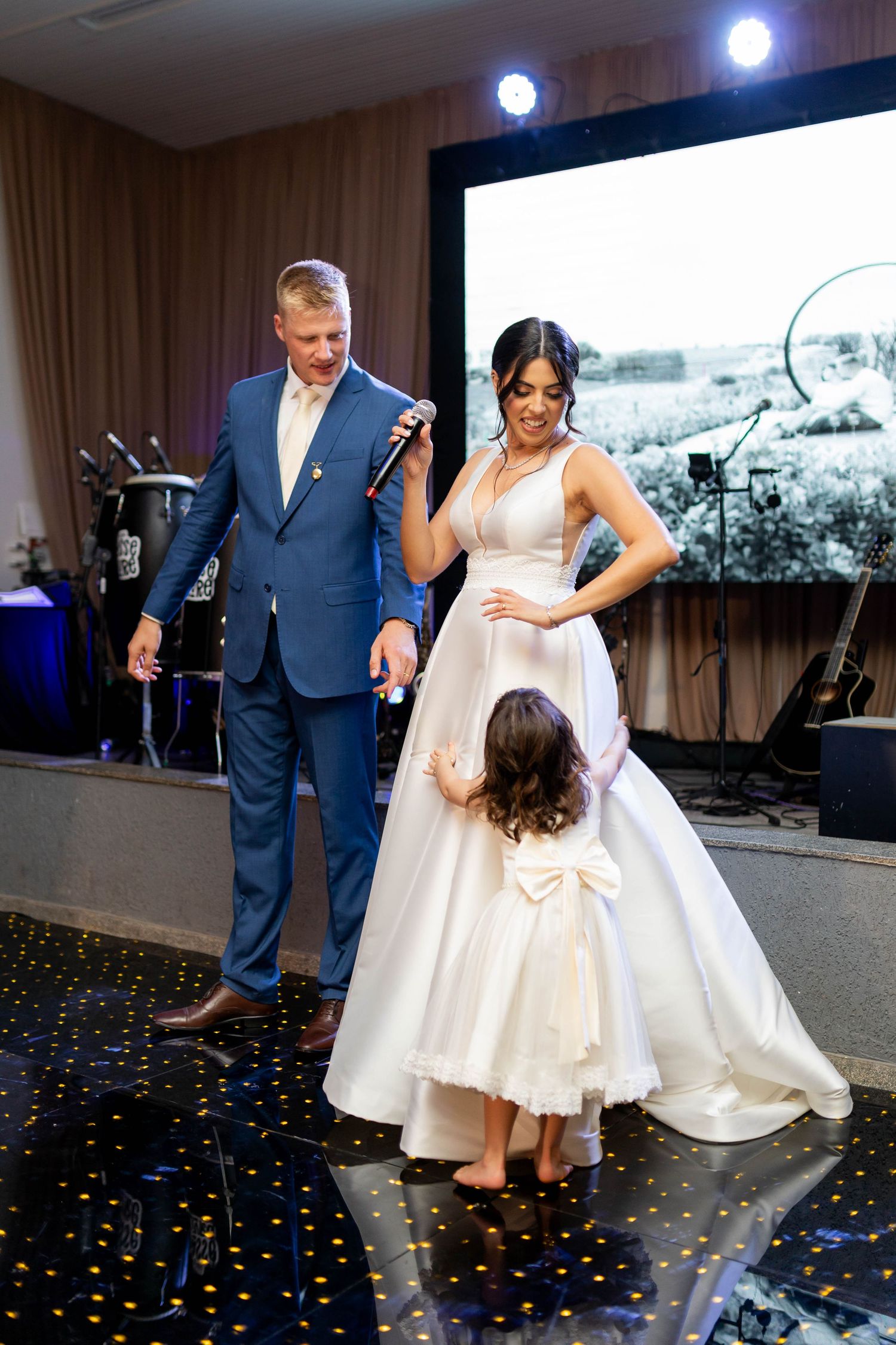 Bride and groom dancing with flower girl at wedding reception on sparkle dance floor.