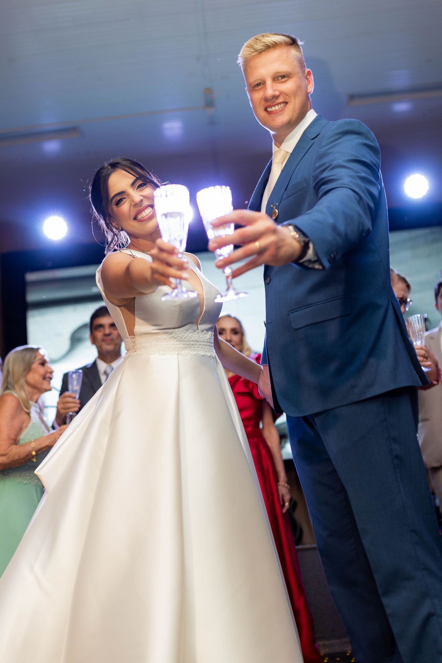 Bride and groom toasting with champagne glasses at wedding reception, smiling couple in white gown and blue suit.