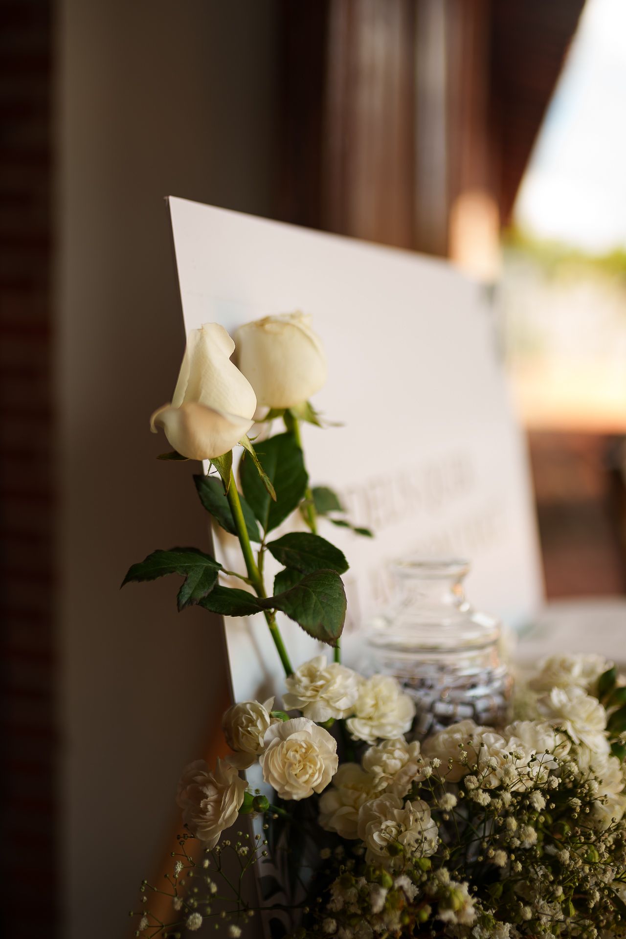 White roses and delicate floral arrangement beside a wedding sign, elegant decor for a romantic ceremony.