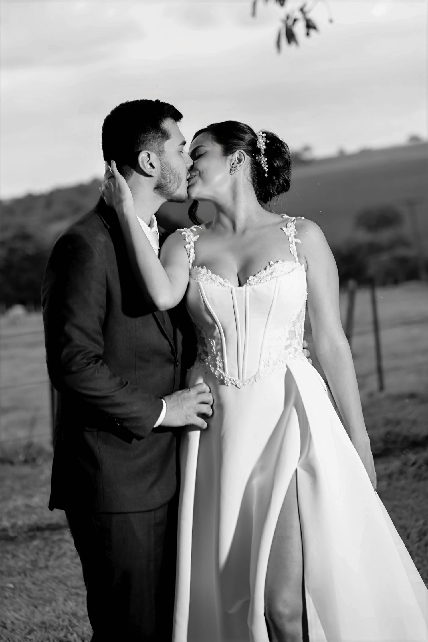 Black and white photo of a bride and groom sharing a romantic kiss outdoors, with rolling hills in the background.