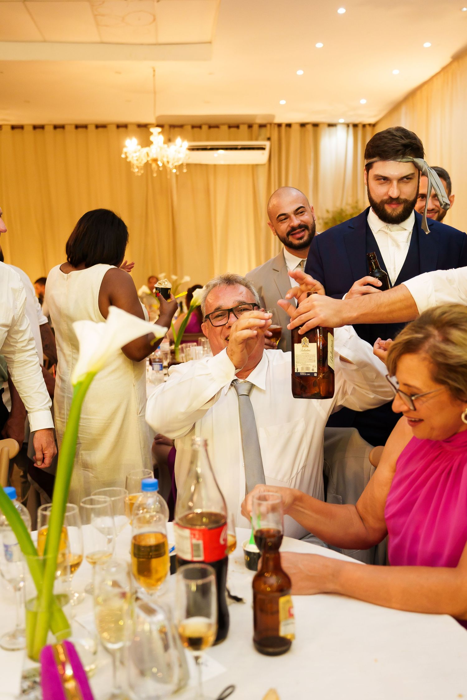 Guests celebrating at a wedding reception, raising glasses and pouring drinks at a decorated banquet table.
