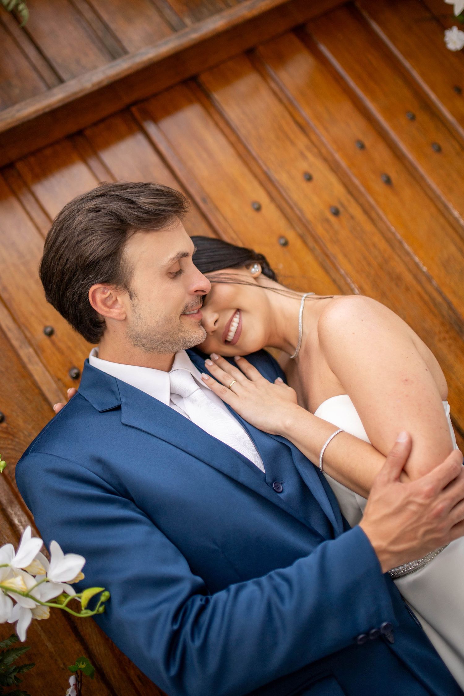 A bride and groom share a tender embrace, smiling together in front of rustic wooden doors on their wedding day.