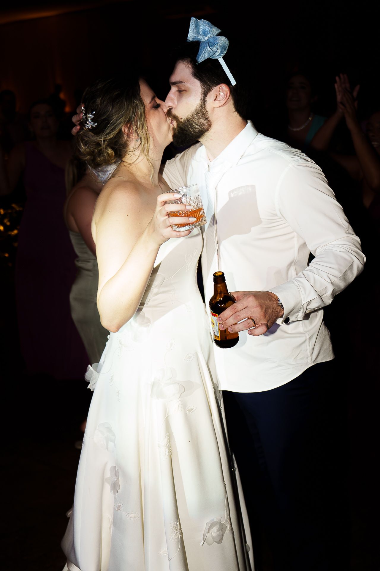 Bride and groom sharing a kiss on the dance floor, holding drinks at their wedding reception.
