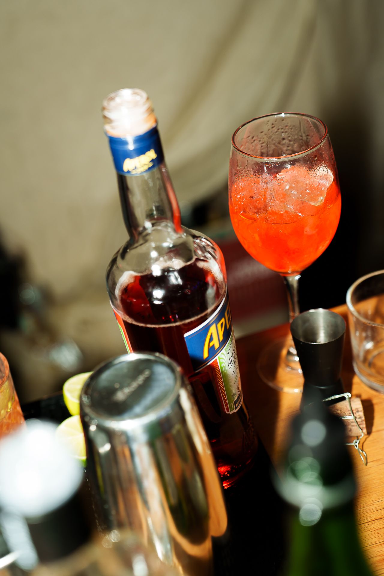 Aperol Spritz cocktail in wine glass with ice beside Aperol bottle on a bar counter.