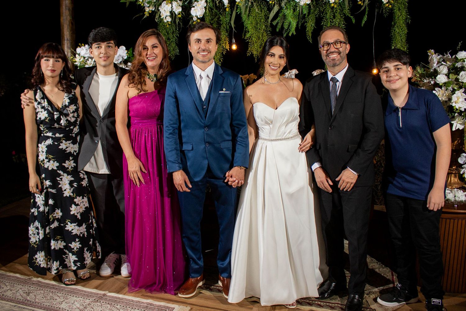 A wedding couple in formal attire poses with family members outdoors at an elegant evening reception.