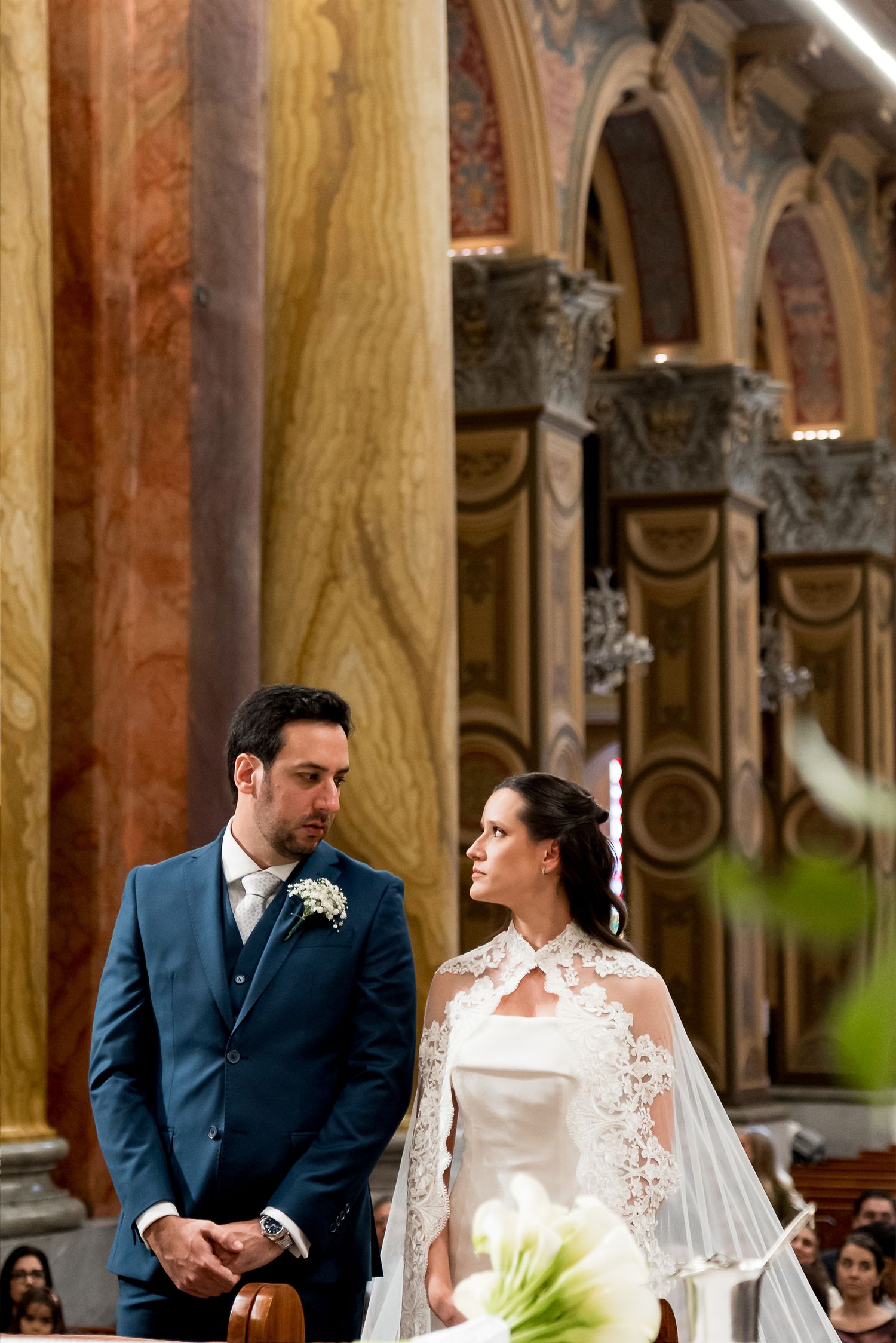Bride and groom stand at the altar in an ornate church during their wedding ceremony, exchanging vows.