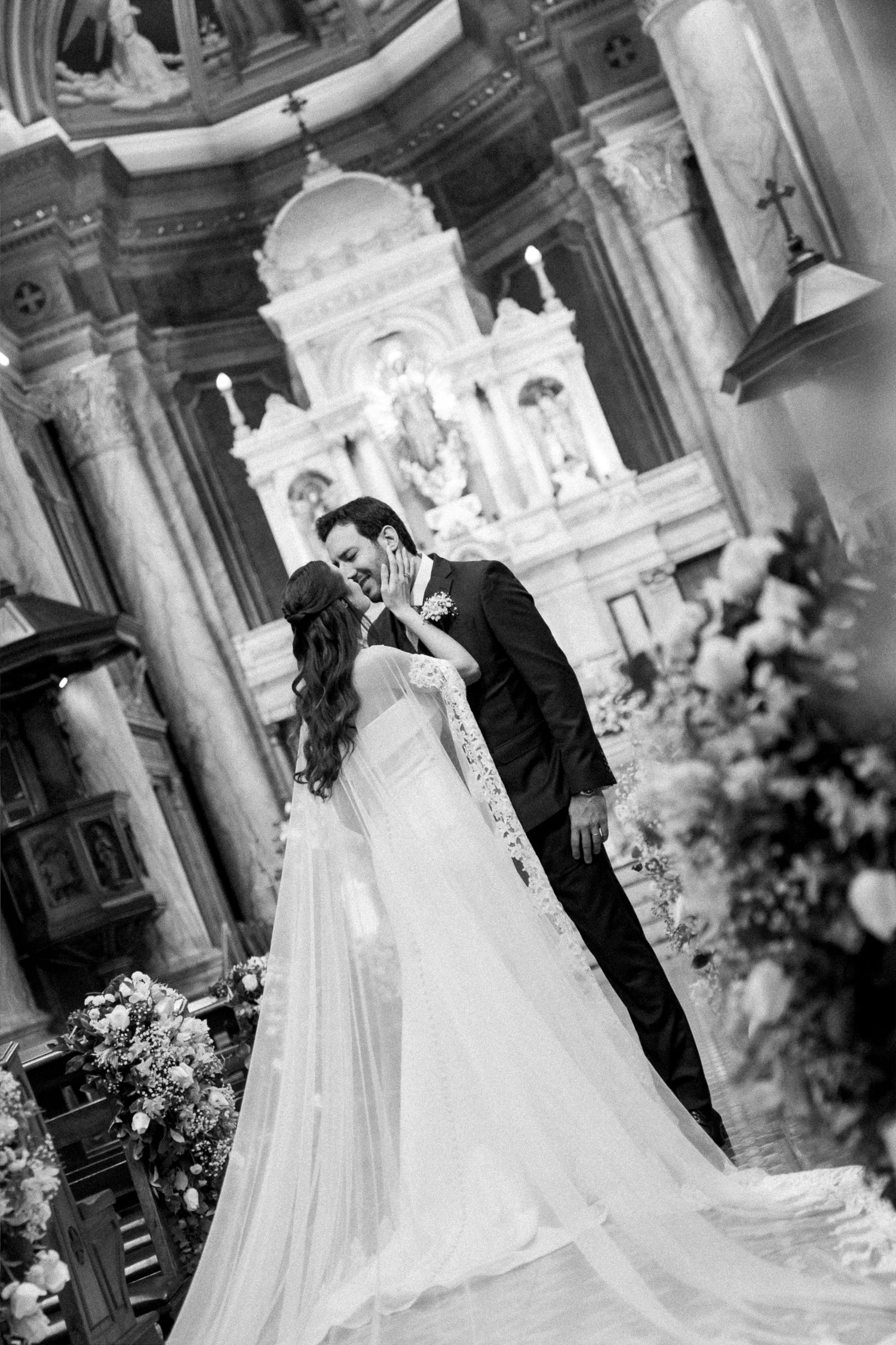 Black and white photo of a bride and groom sharing a kiss at the altar of an ornate church.