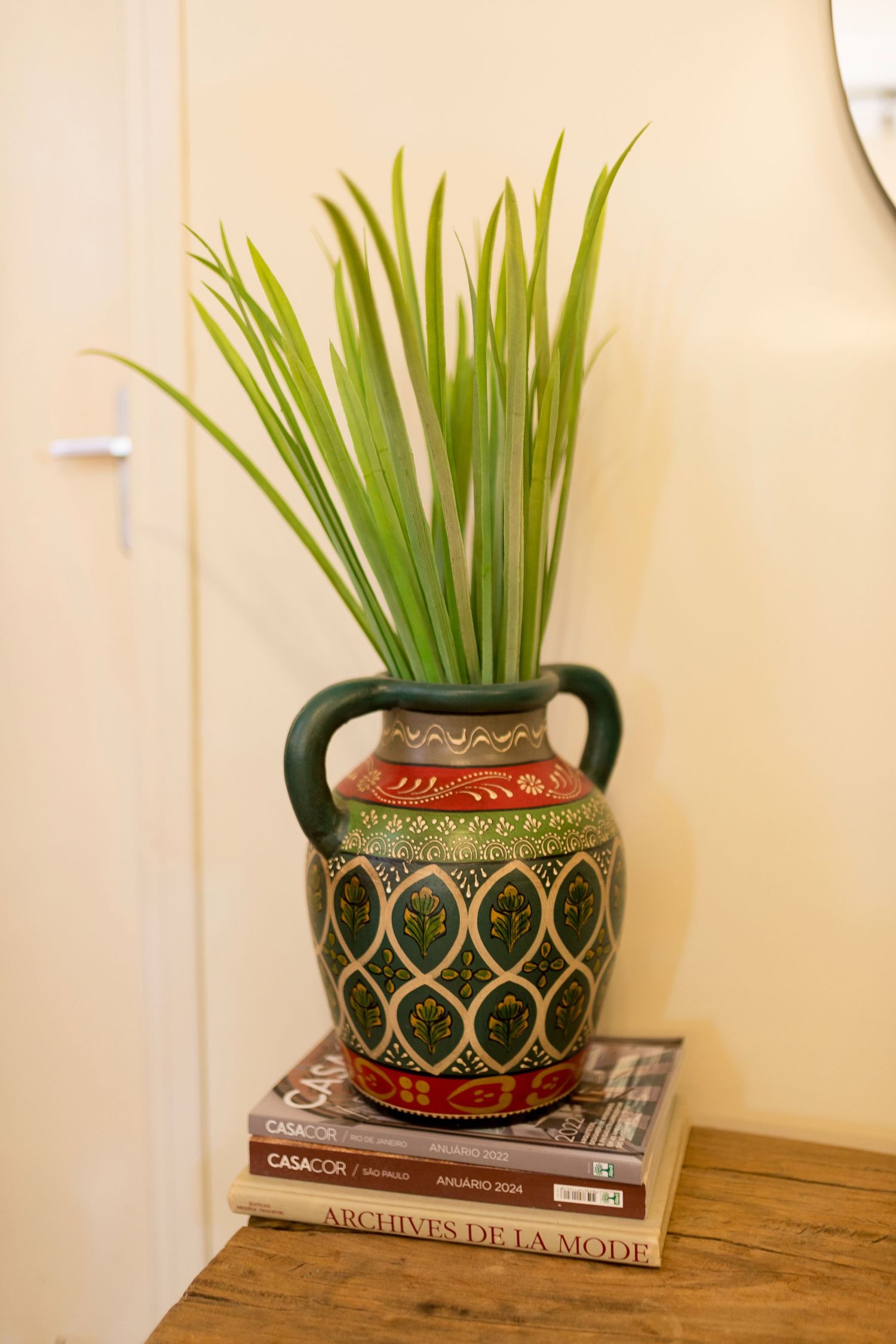 Decorative Moroccan-style ceramic vase with green plants on stacked books atop a wooden table.