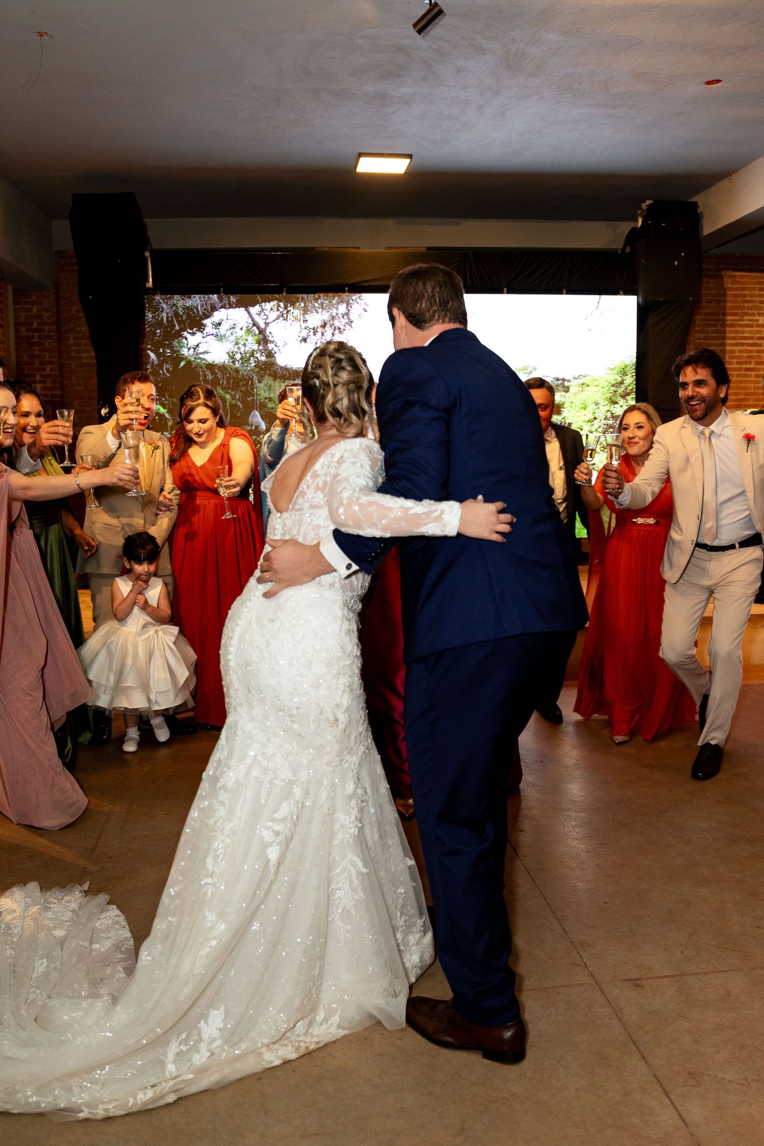 Bride and groom share their first dance surrounded by smiling guests in red and white attire at an elegant wedding reception.