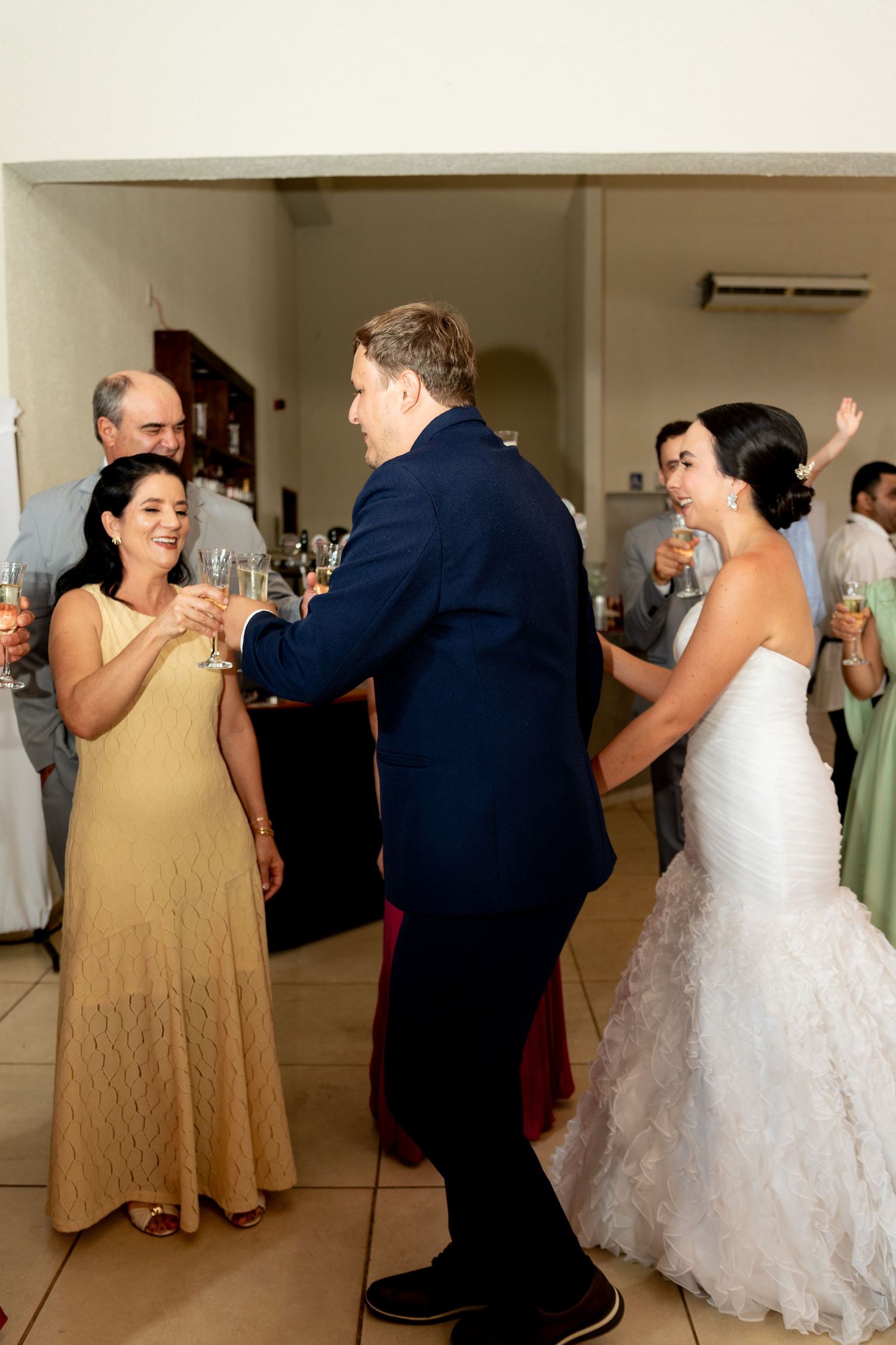 Bride in white gown and groom in navy suit share a toast with guests at elegant wedding reception.
