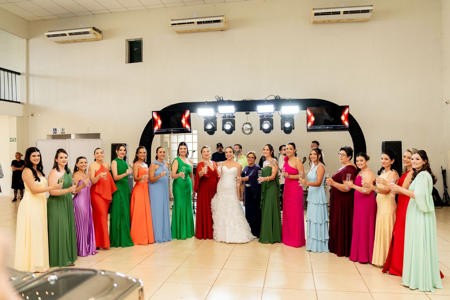 Bride in white gown poses with colorful bridesmaids in rainbow dresses at elegant wedding reception venue.