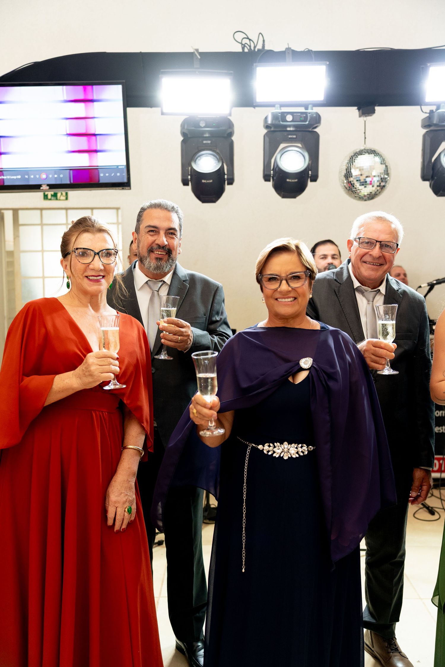 Four elegantly dressed adults toasting with champagne glasses at a formal event under bright stage lights.