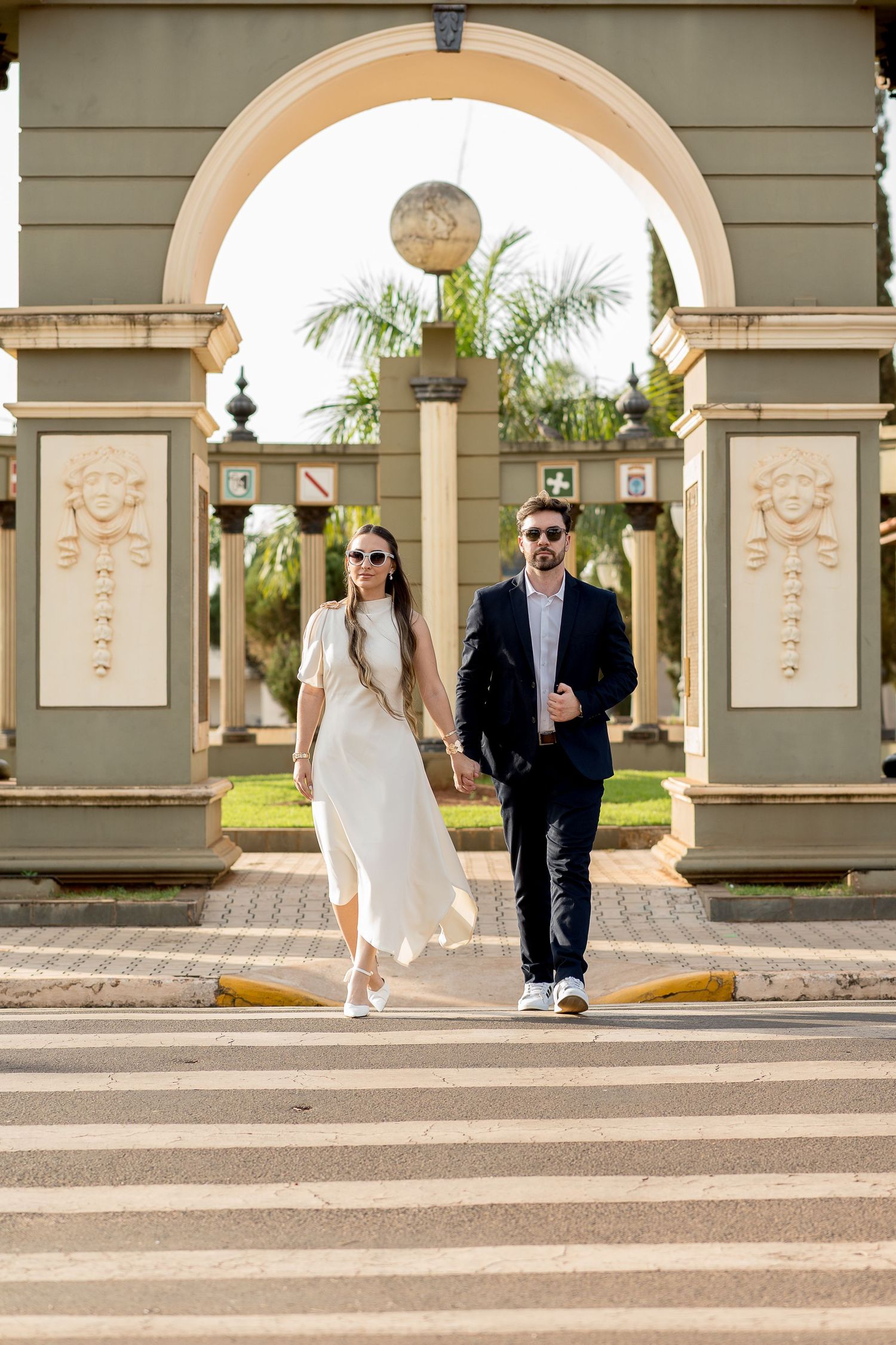 Elegant couple walking hand in hand through an ornate archway entrance, woman in white dress, man in dark suit.