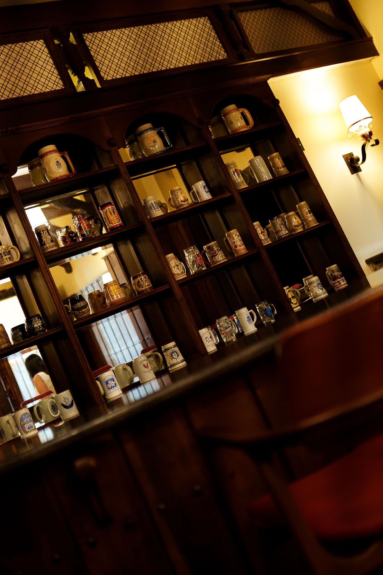 Warm wooden bar shelves displaying a large collection of vintage beer steins and mugs in a cozy pub setting.