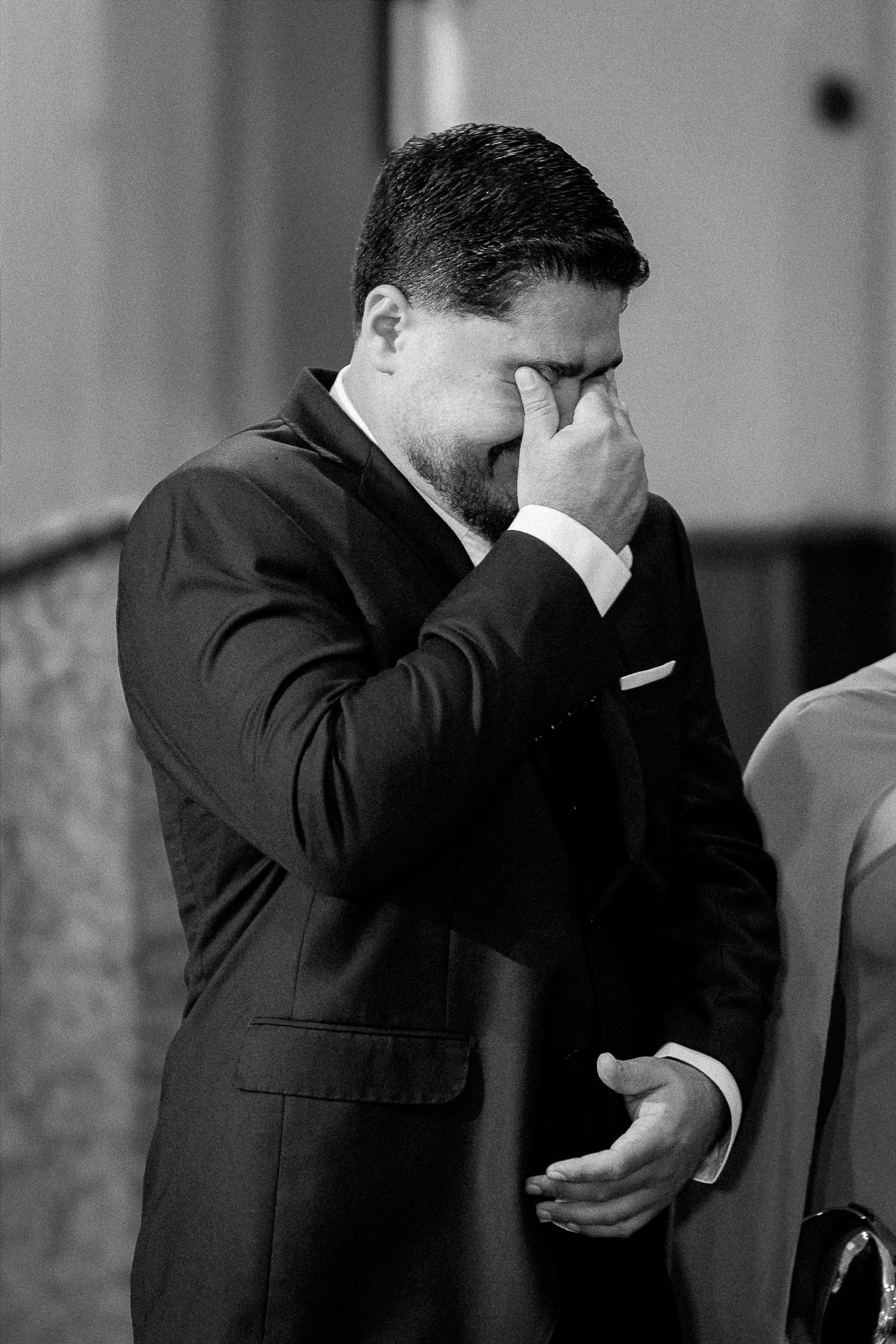 Emotional groom wiping tears during wedding ceremony in black and white photo.