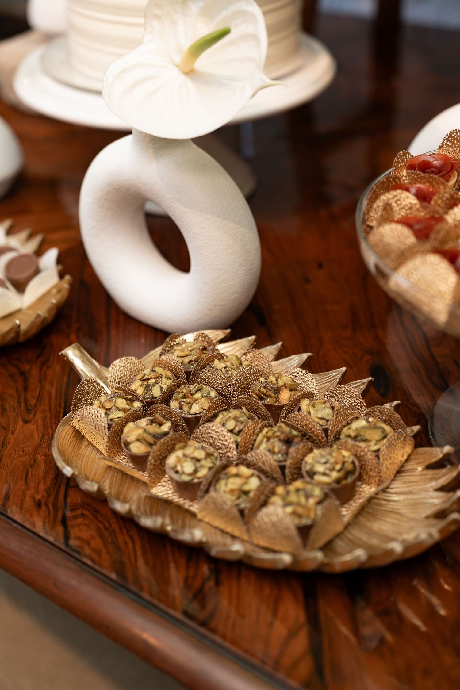 Gold leaf tray with pistachio filled pastry cones displayed on a wooden table with white ceramic decor.
