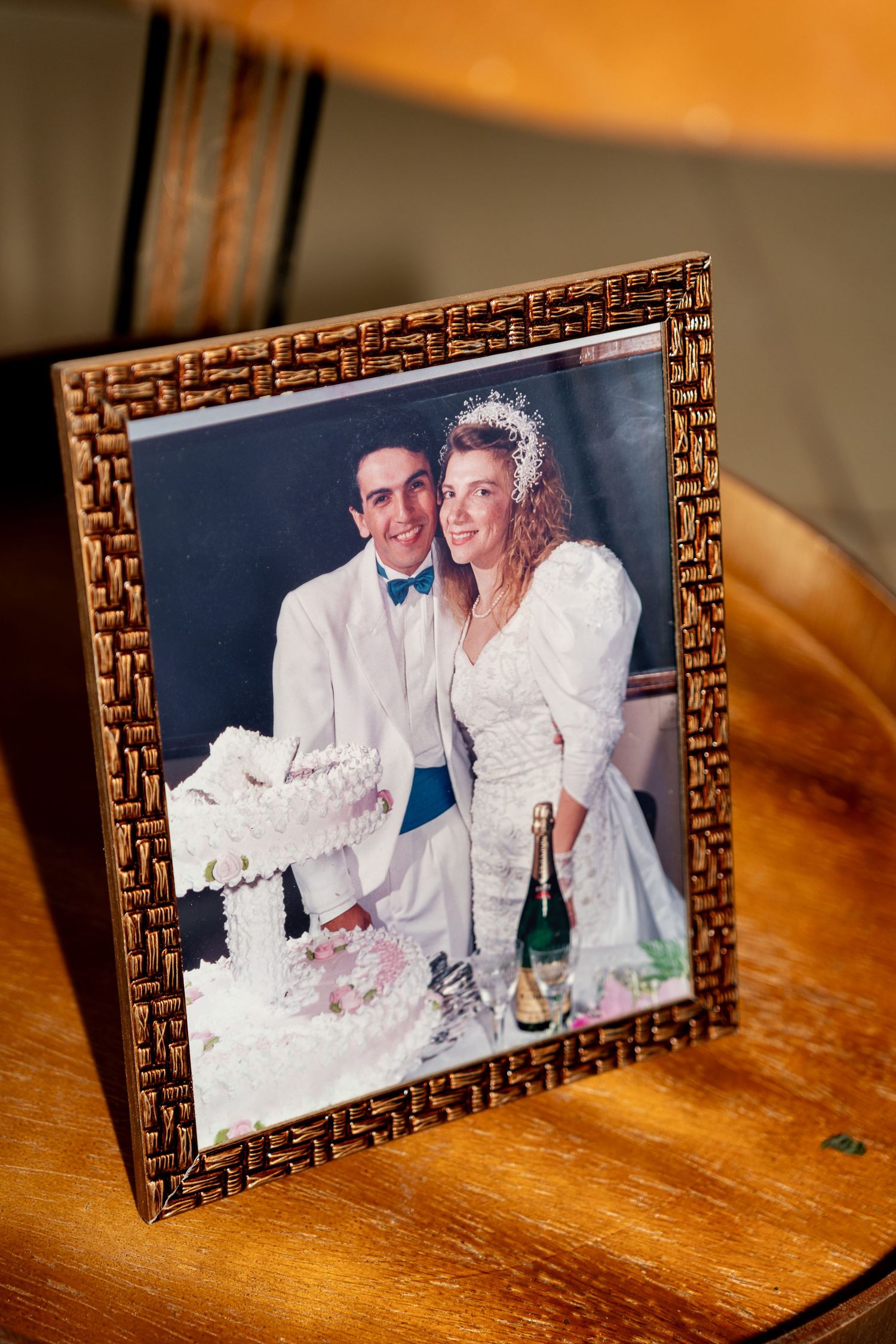 Framed vintage wedding photo of bride and groom cutting cake with champagne bottle, displayed on wooden table.