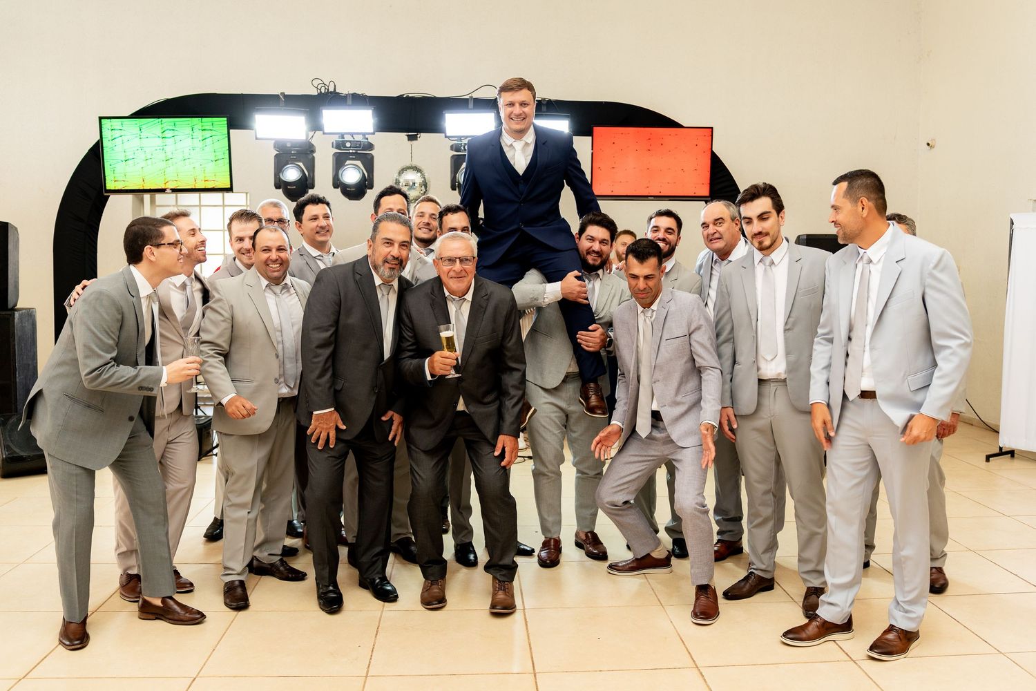 Group of men in gray suits celebrating, lifting one man on their shoulders at a formal event.