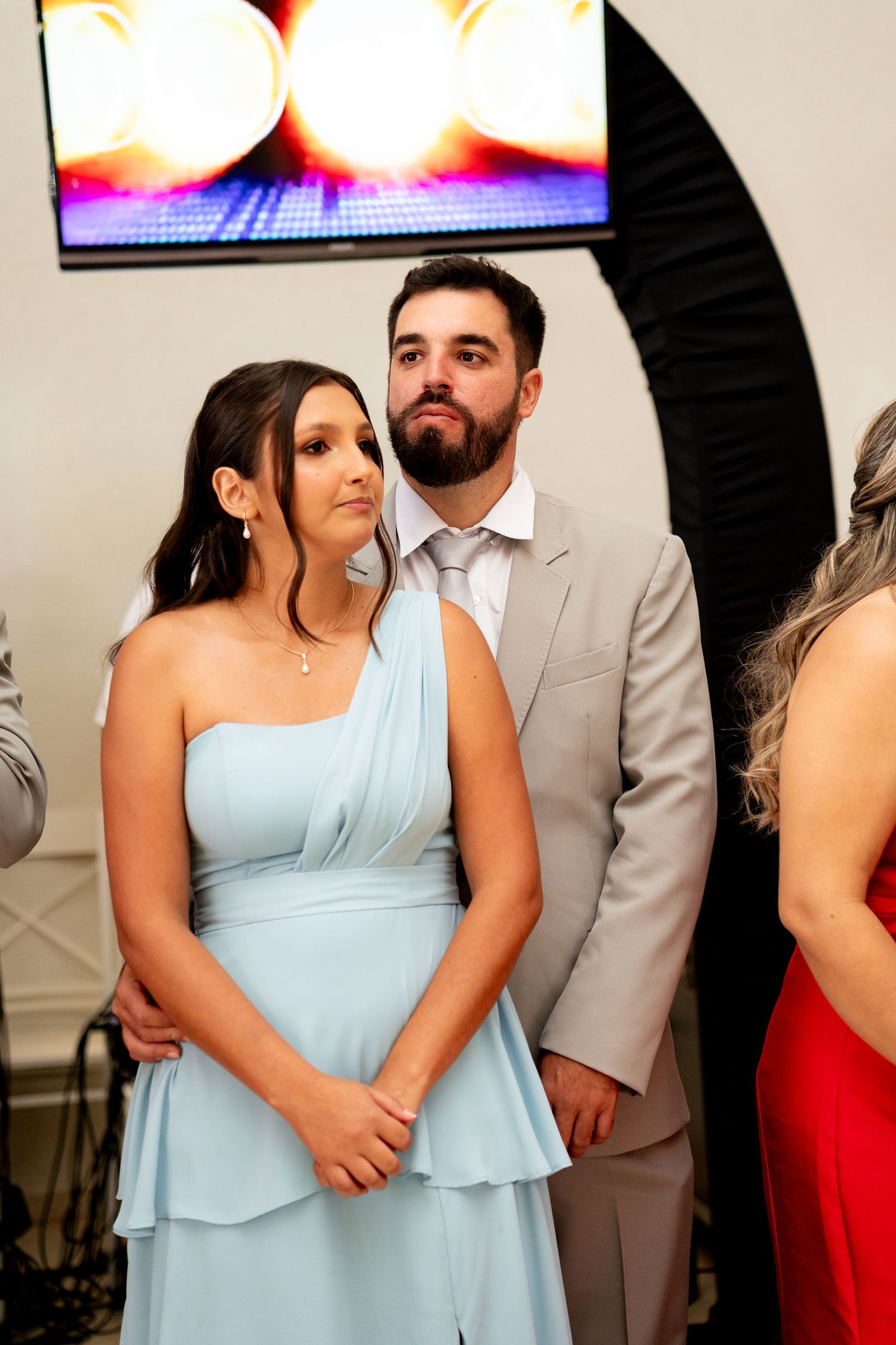 Couple in formal attire, woman in light blue one-shoulder dress, man in gray suit, posing at an elegant event.