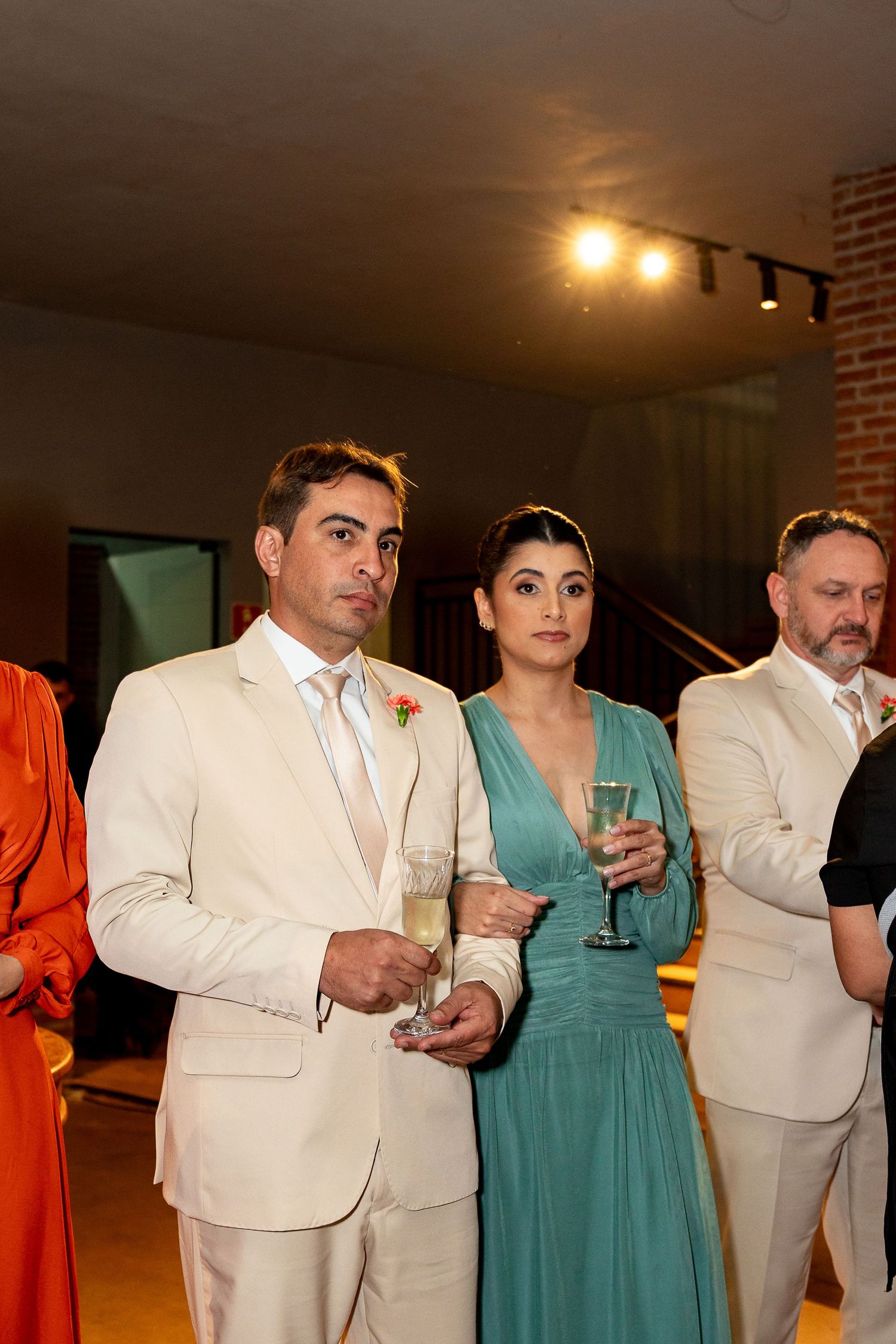 Elegantly dressed couple holding champagne glasses at a formal wedding reception event.