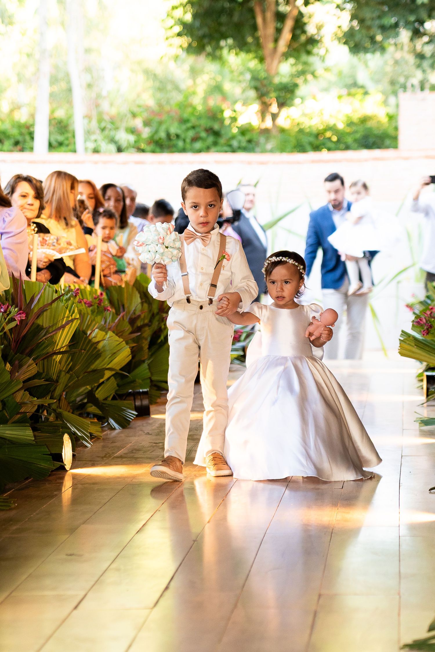 Ring bearer and flower girl walking down the aisle at an elegant outdoor wedding ceremony.