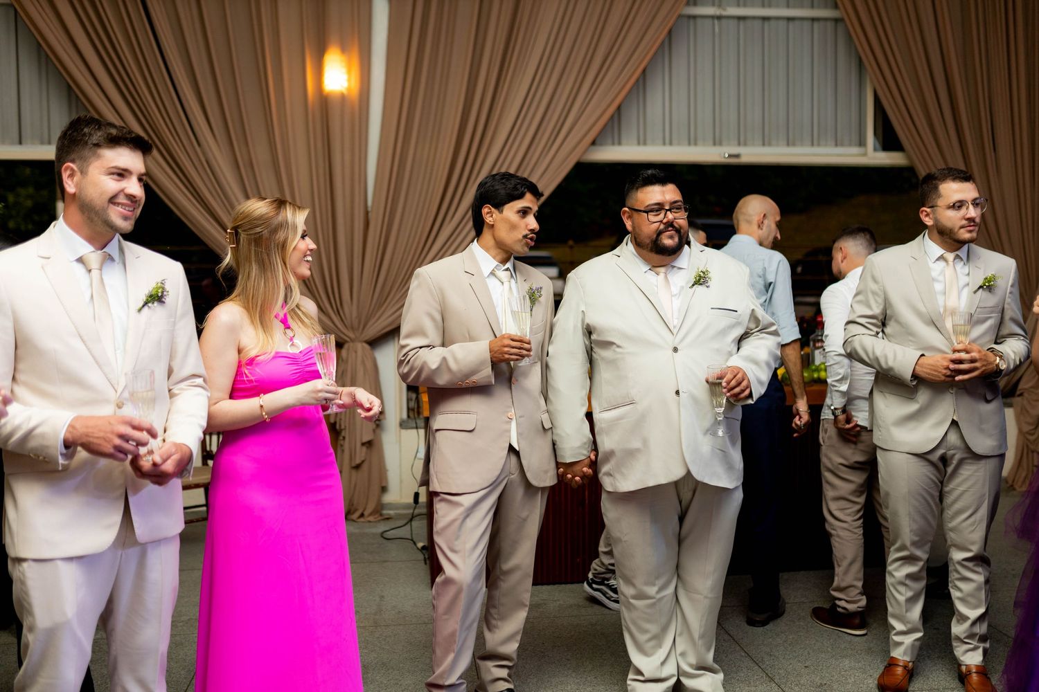 Wedding guests in formal attire socializing at an elegant indoor reception venue with draped curtains.