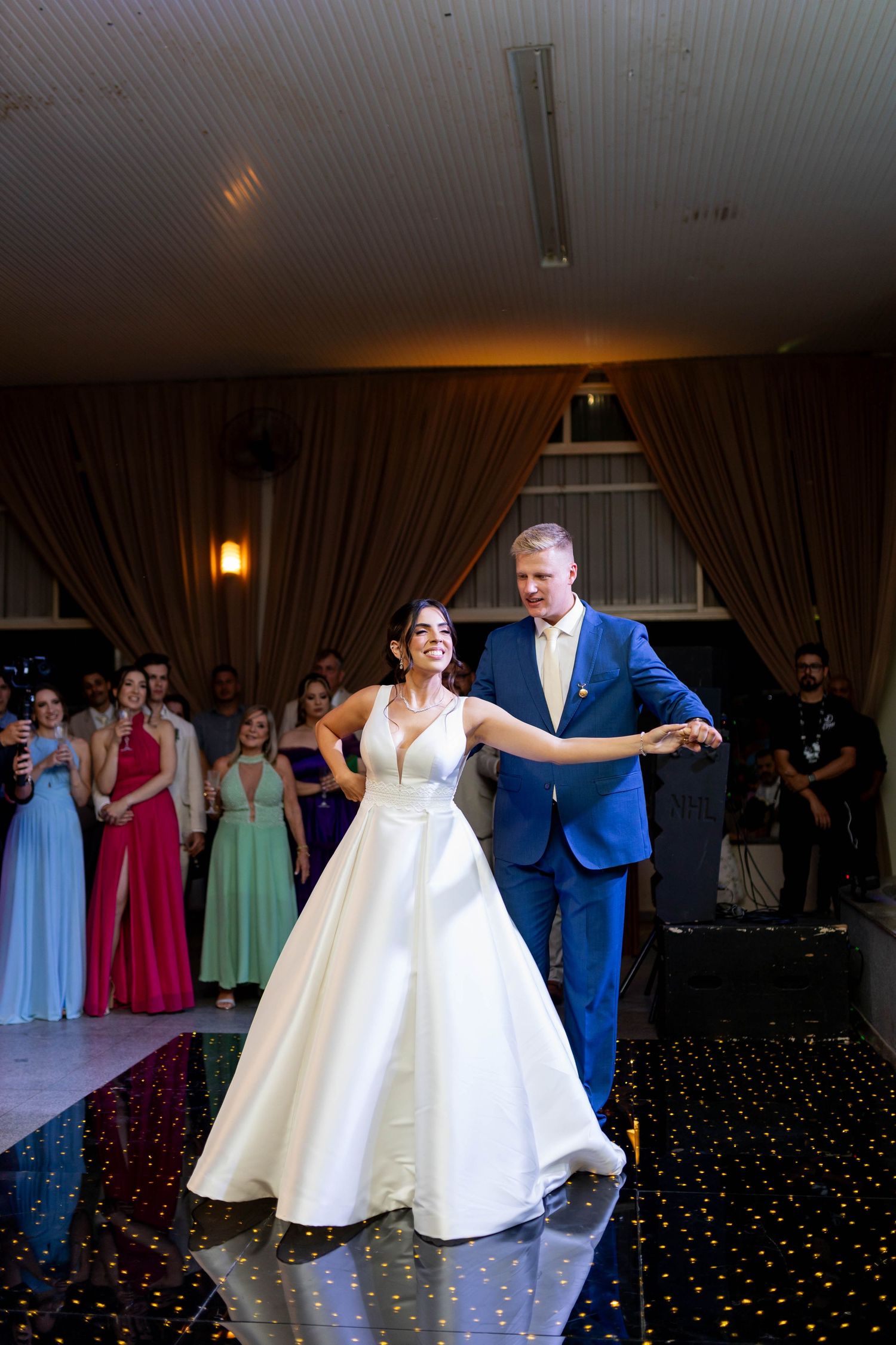 Bride and groom share their first dance on a starlit floor, surrounded by guests at an elegant wedding reception.