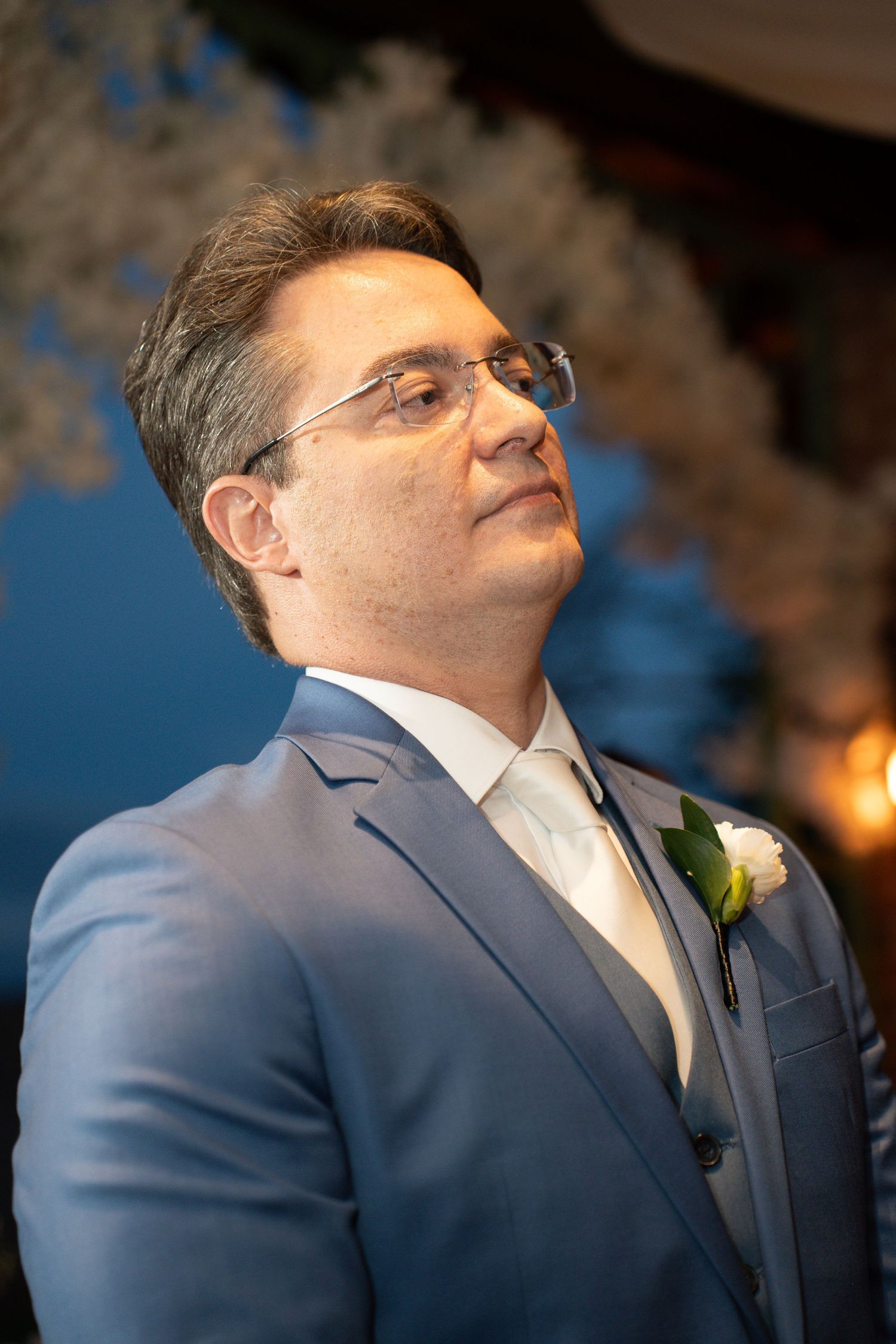 A groom in a blue suit with boutonniere gazes forward at his wedding ceremony.