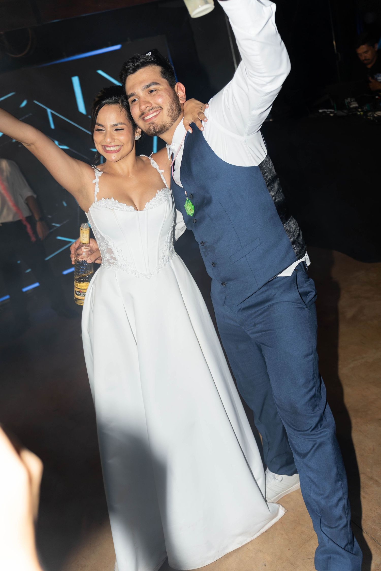 A joyful bride in a white gown and groom in a blue suit celebrate their wedding reception on the dance floor.