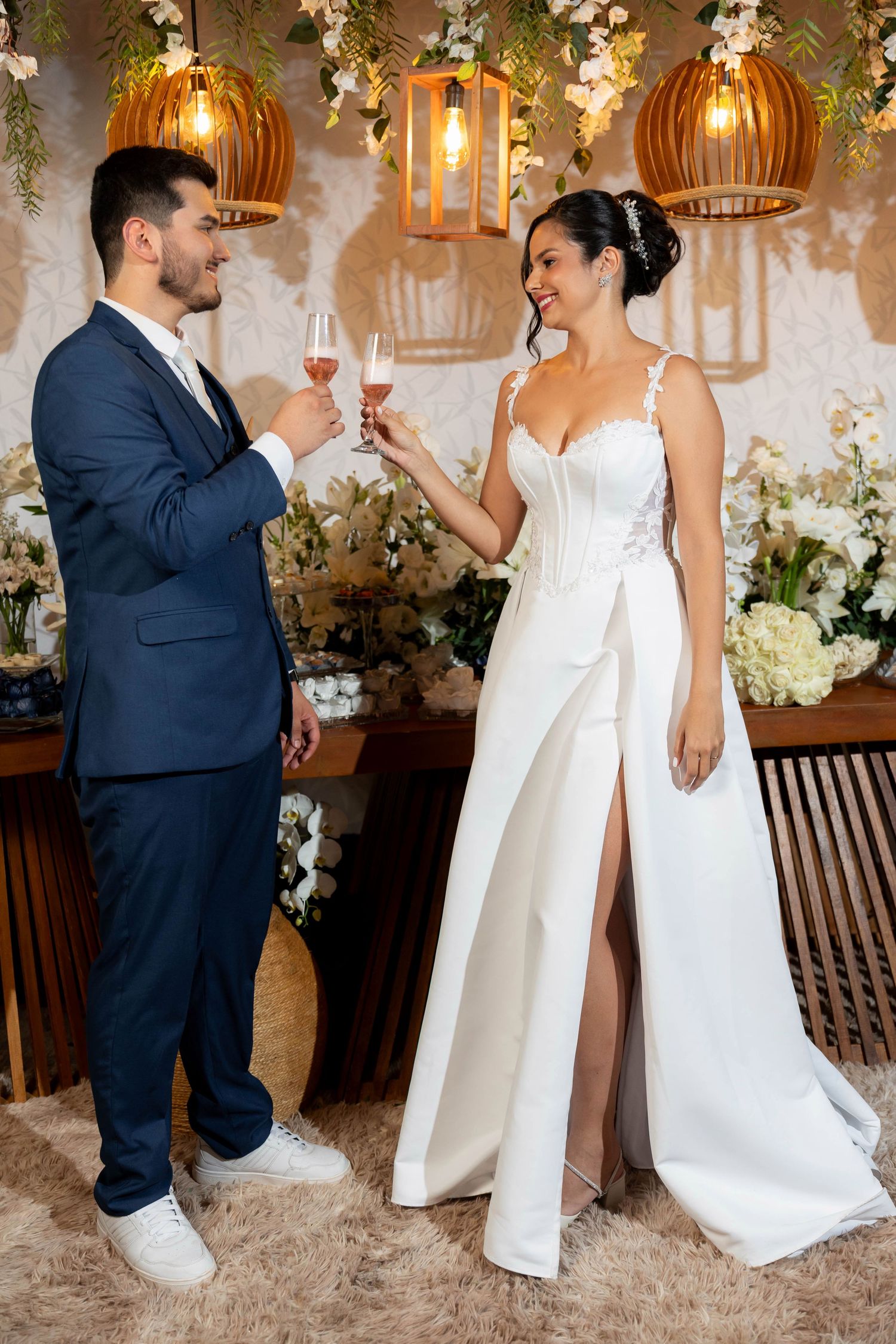 Bride and groom toasting with champagne glasses at their elegant wedding reception, surrounded by floral decorations and warm lighting.