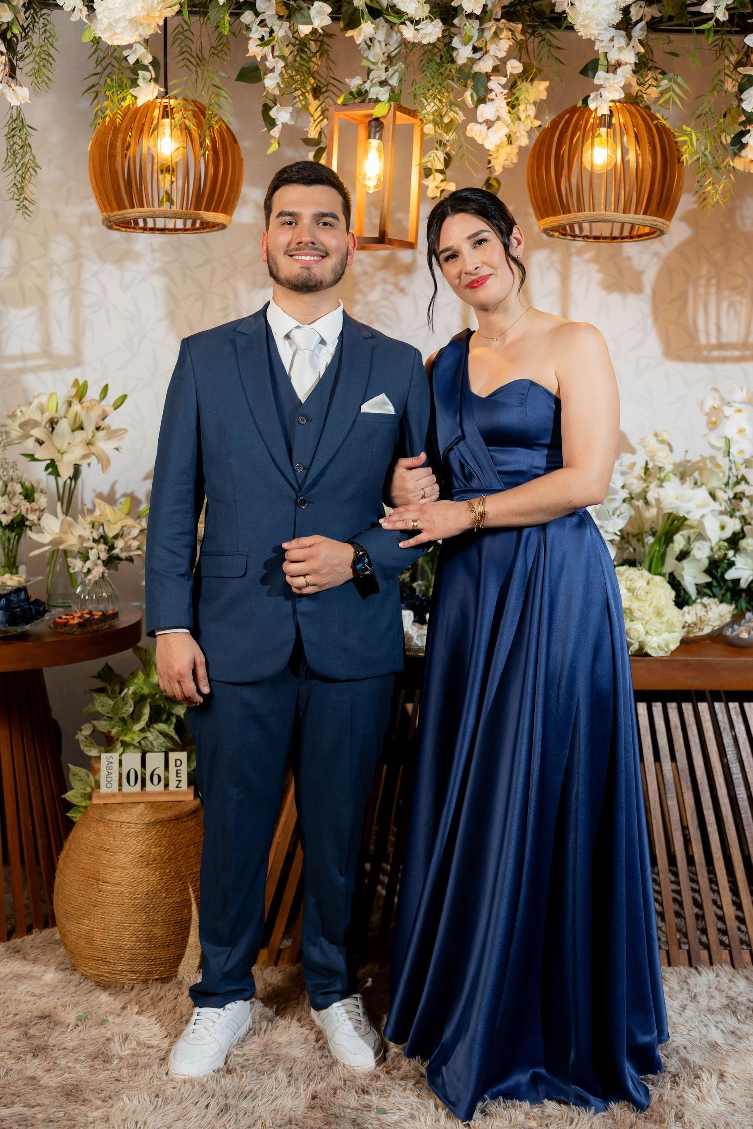 Couple in matching navy blue formal attire posing together at an elegant floral decorated event venue.