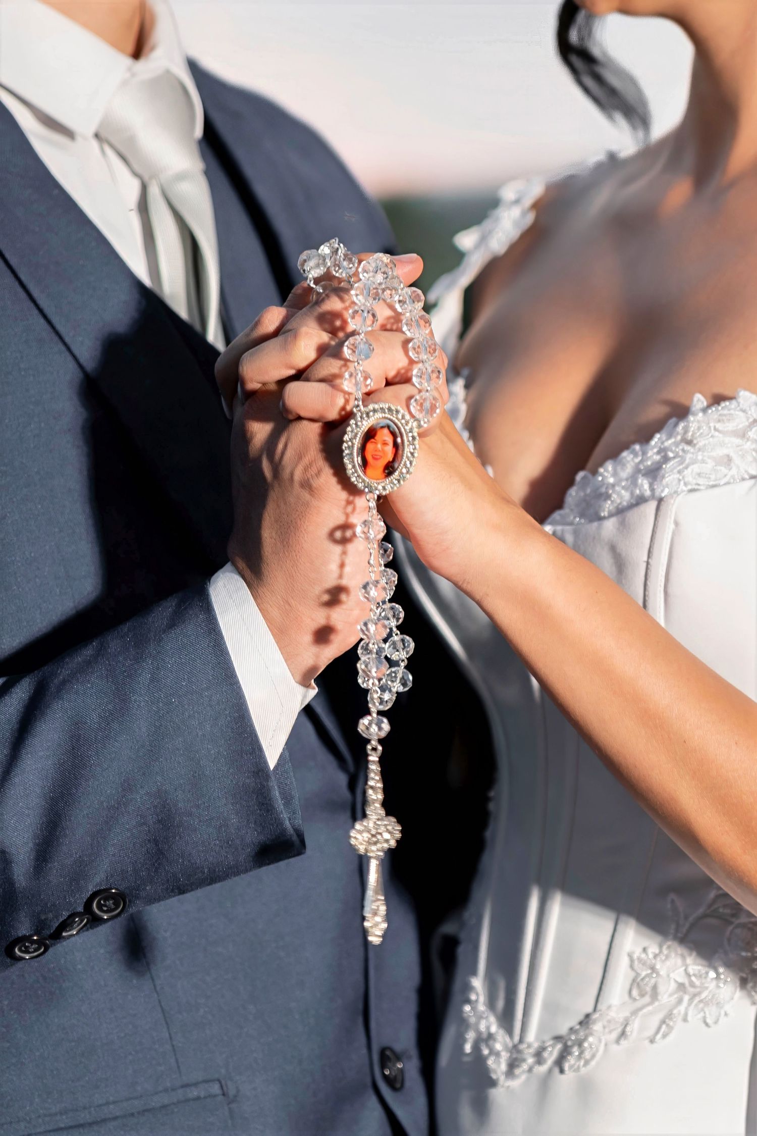 Bride and groom holding a crystal rosary with orange gemstone centerpiece at wedding ceremony.