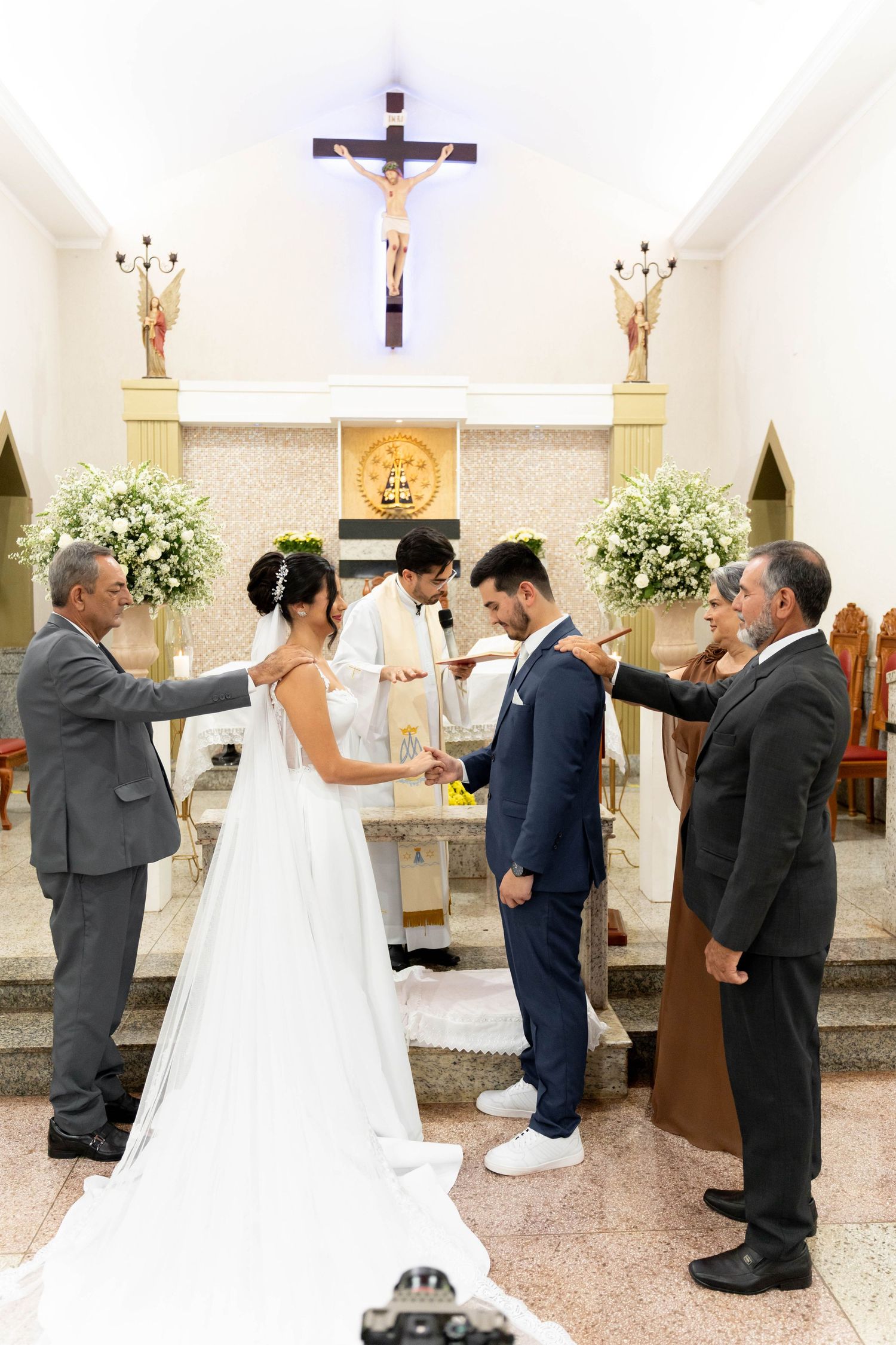 Bride and groom exchange vows at a Catholic church altar, flanked by family members during a wedding ceremony.