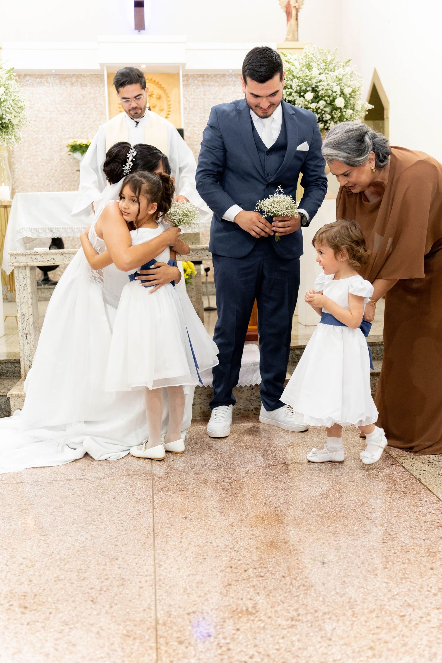 Bride and groom with flower girls and elderly woman celebrating wedding ceremony inside a church.
