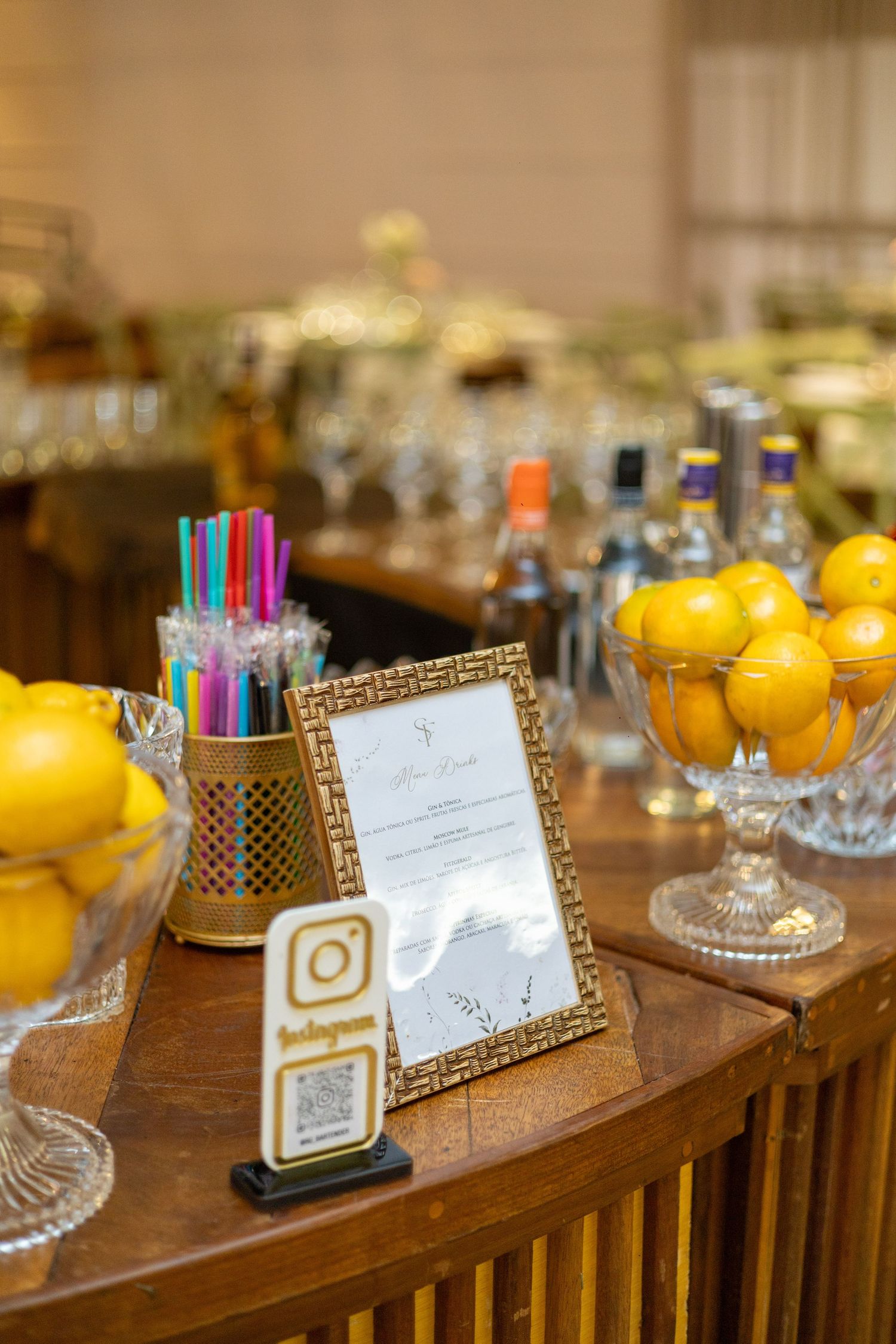 Elegant bar setup with lemons, colorful straws, liquor bottles, and a framed menu sign on wood counter.