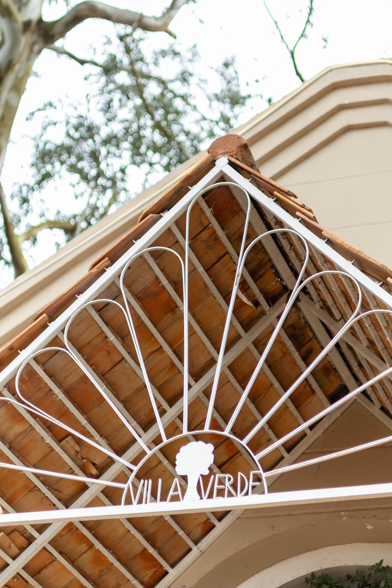 White ornate iron gate with Villa Verde sign at entrance of a charming villa with terracotta roof tiles.
